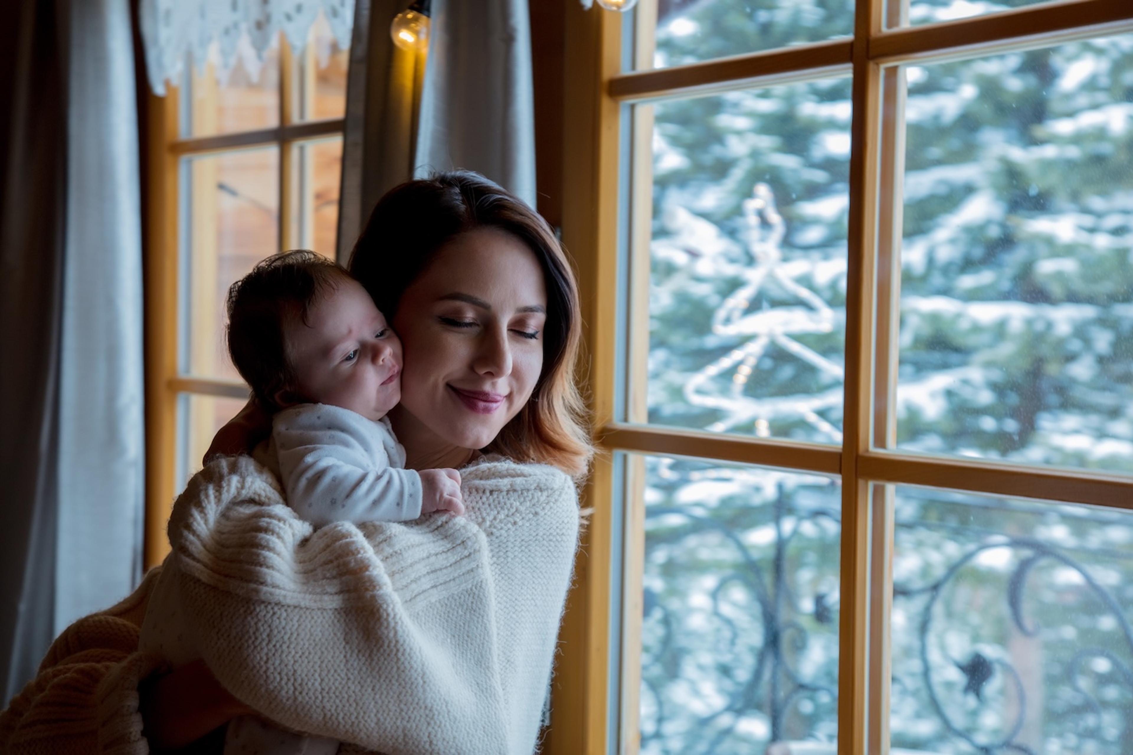 Mom holds newborn baby near window on a snowy winter day