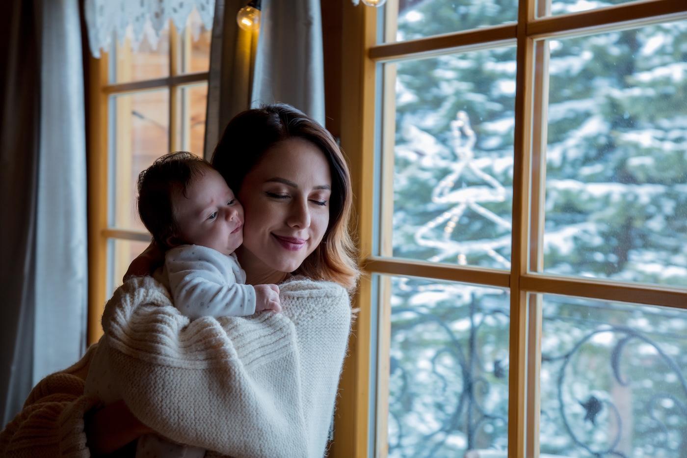 Mom holds newborn baby near window on a snowy winter day