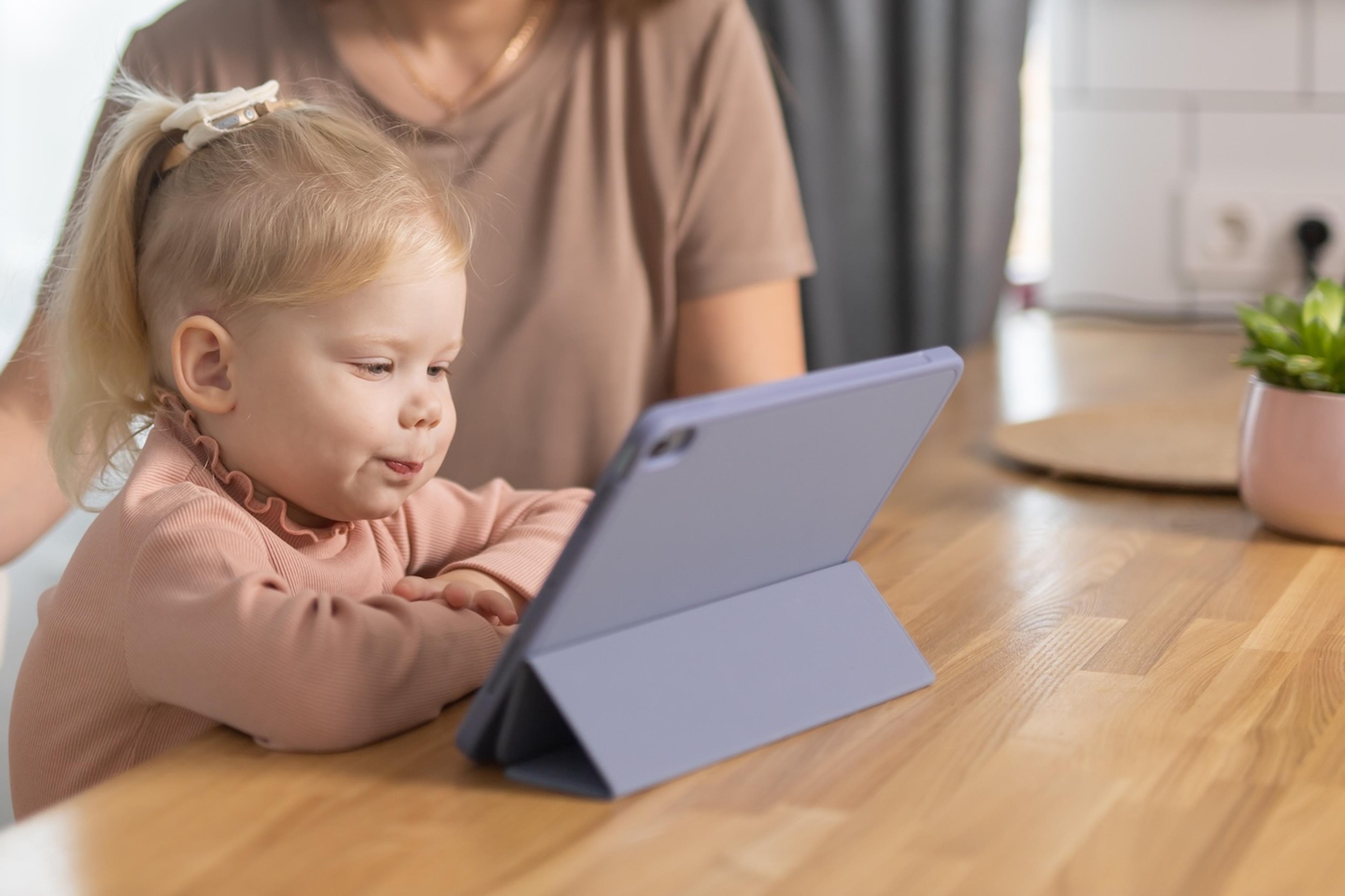 A toddler looks at an iPad while her mother watches