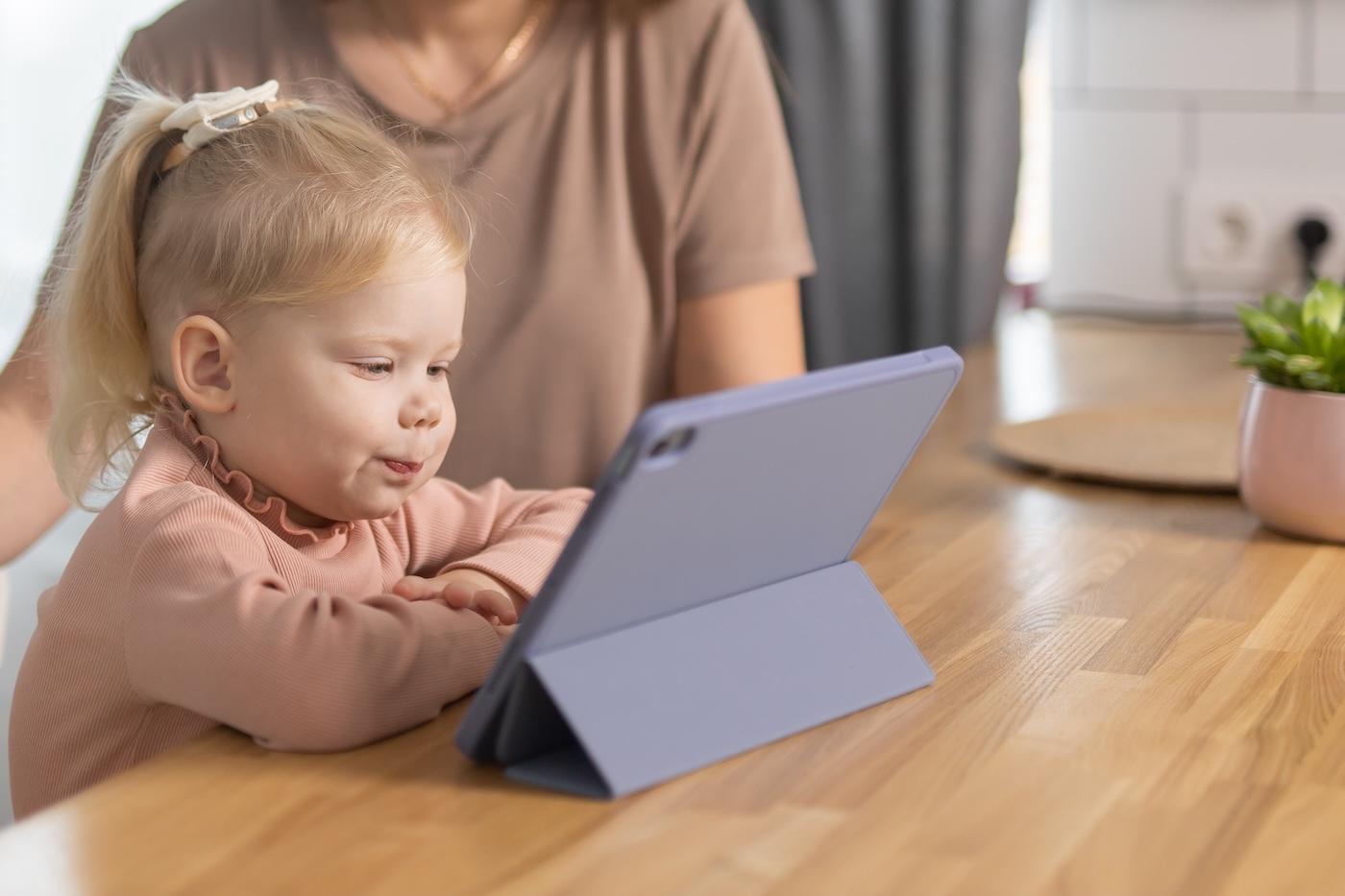 A toddler looks at an iPad while her mother watches