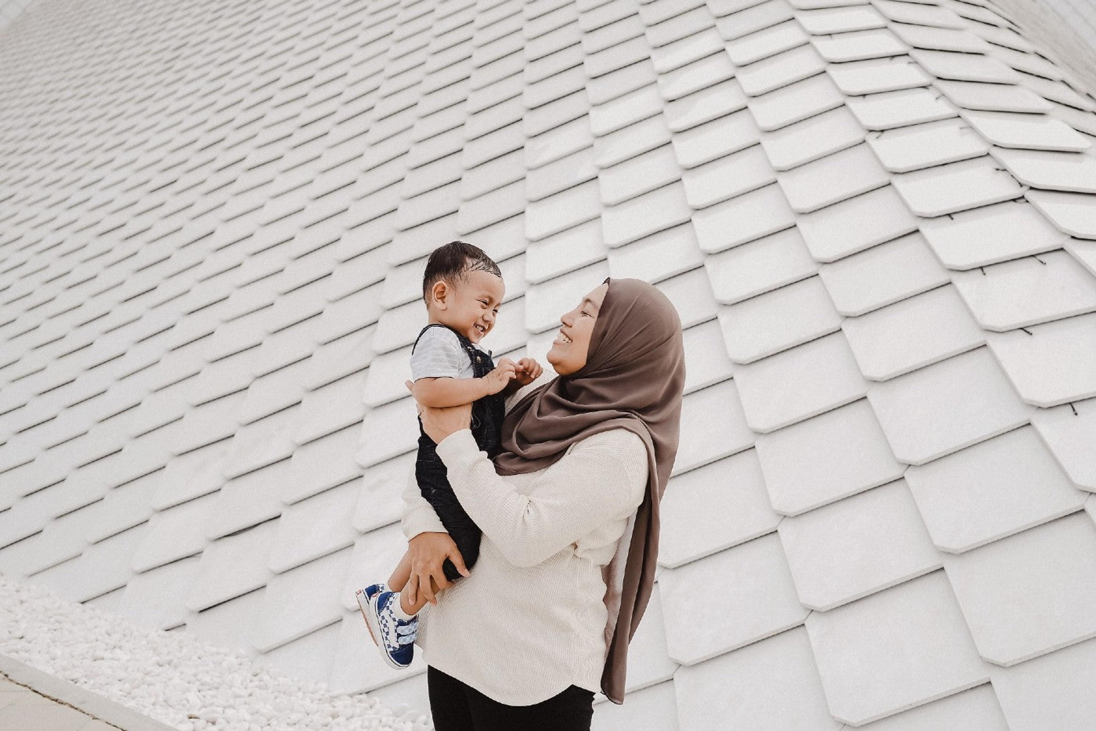 Mother in head scarf holding and smiling at toddler son.