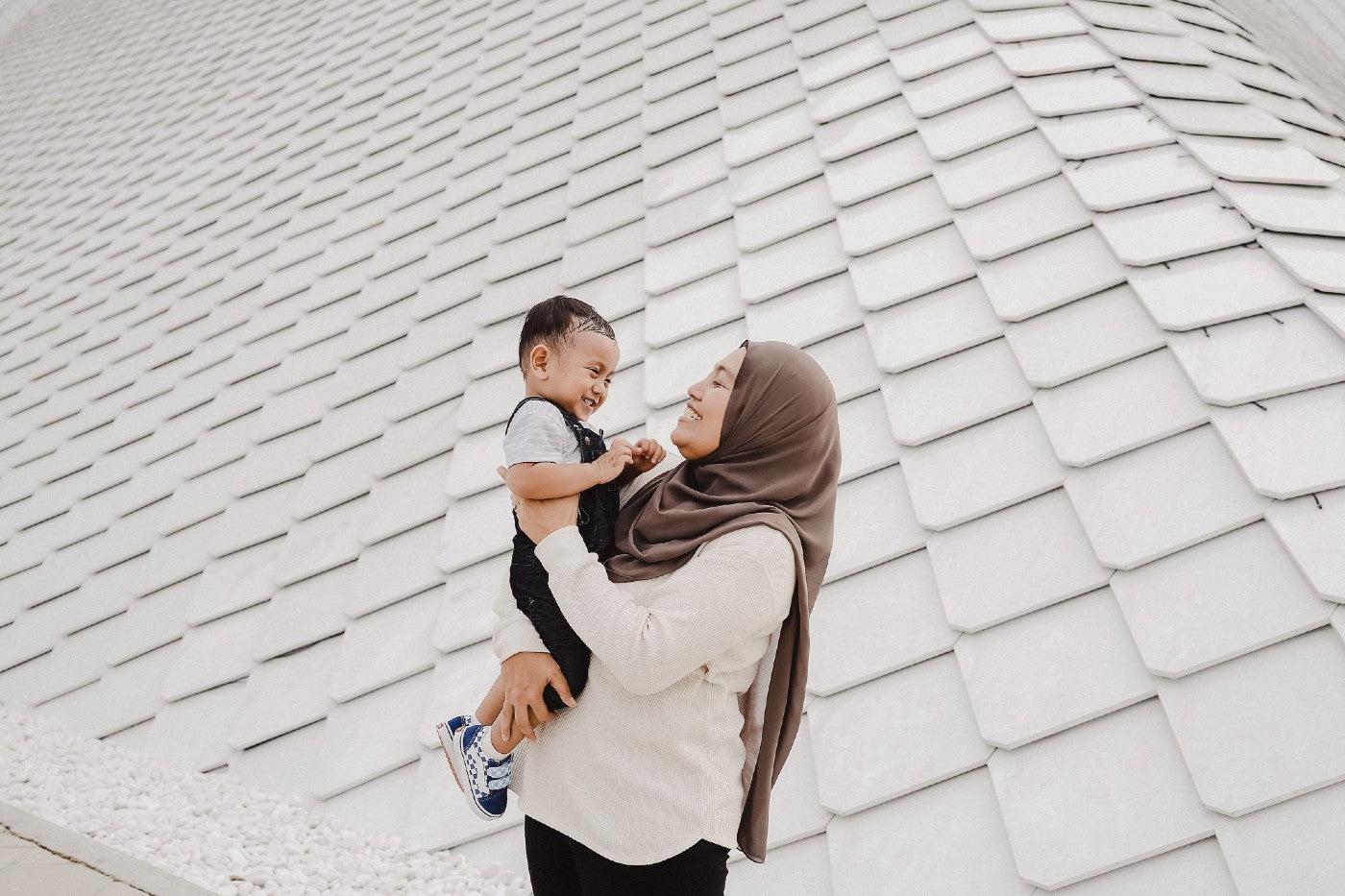 Mother in head scarf holding and smiling at toddler son.