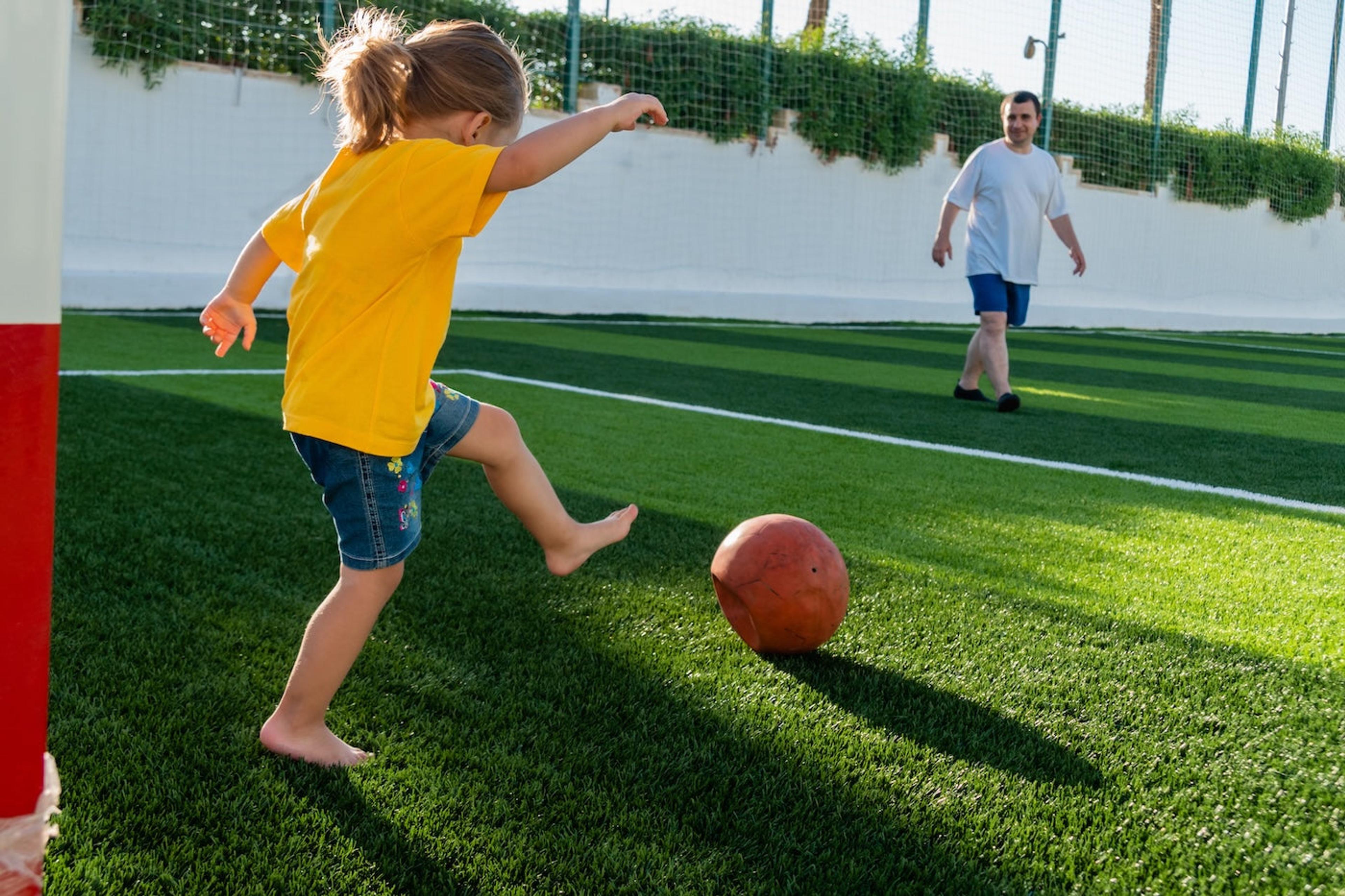 A little girl kicks a ball on artificial turf