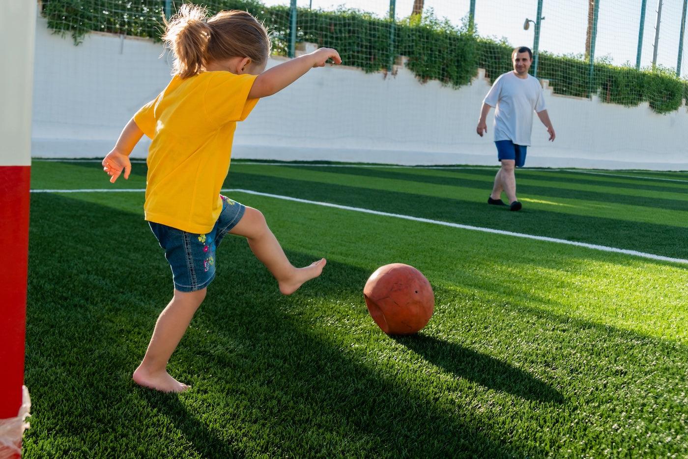 A little girl kicks a ball on artificial turf