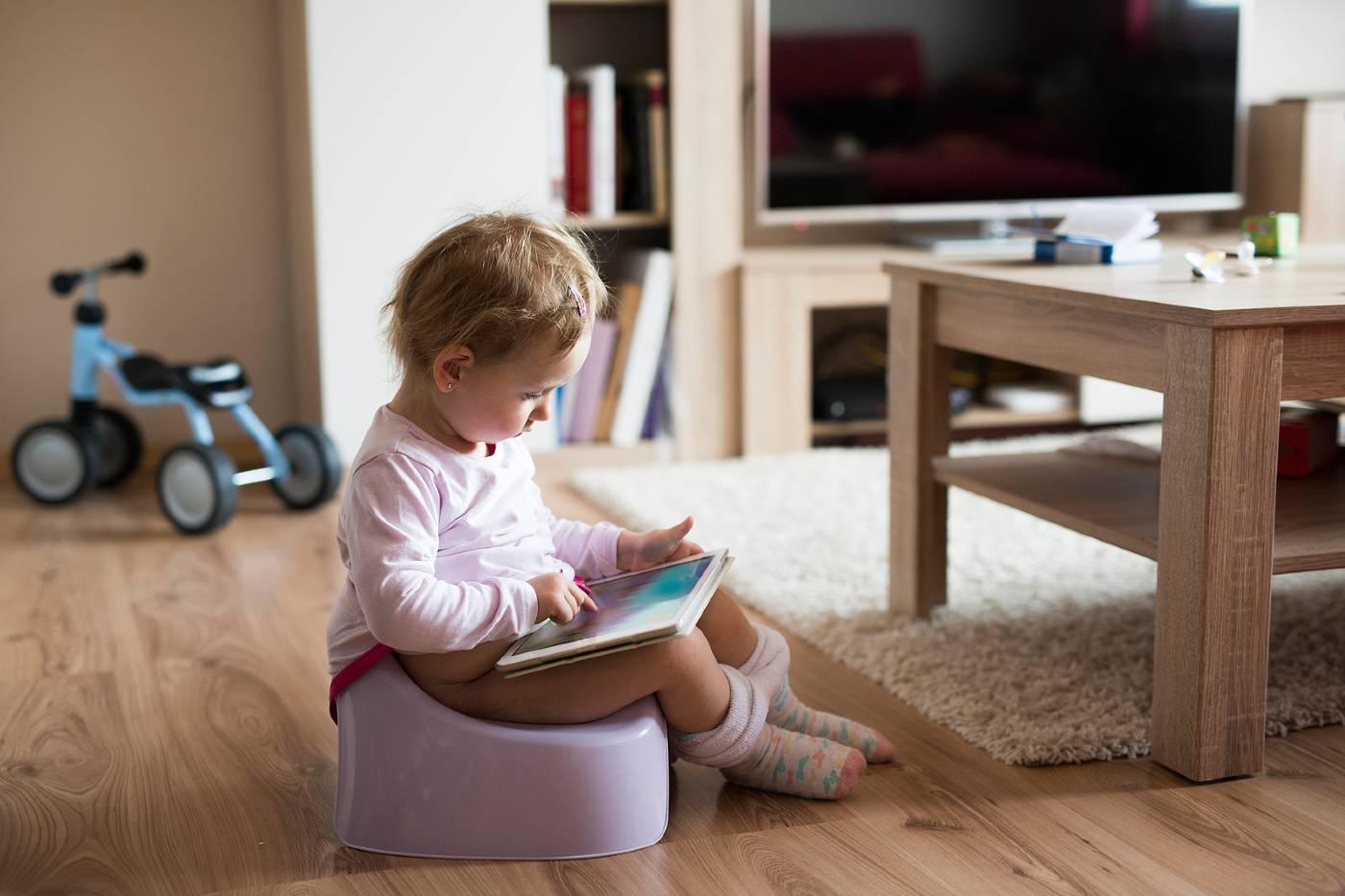 A constipated toddler sits on the potty with a book