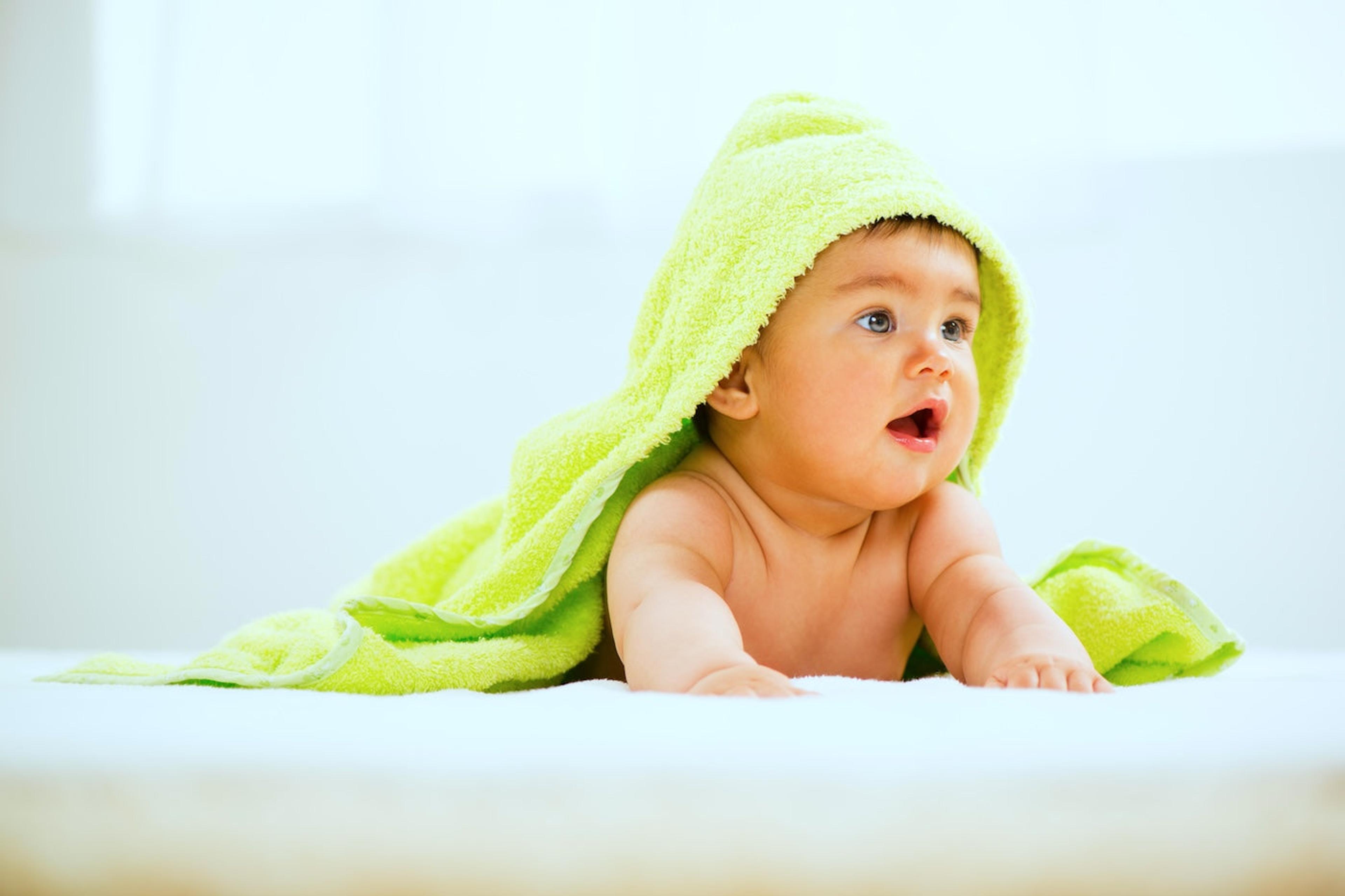 Baby on belly wearing bright green hooded towel