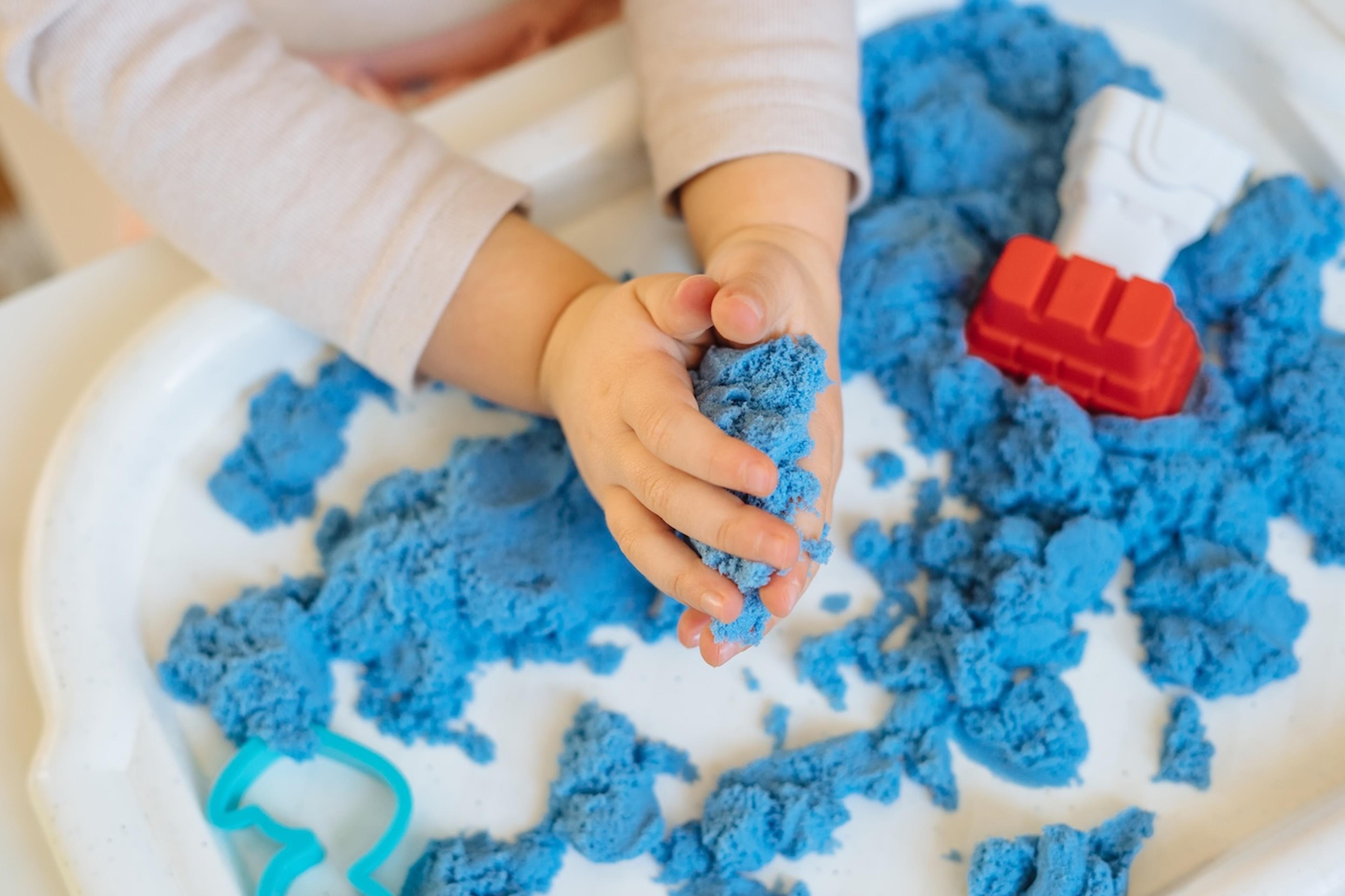 A toddler squishes blue kinetic sand during a sensory play activity