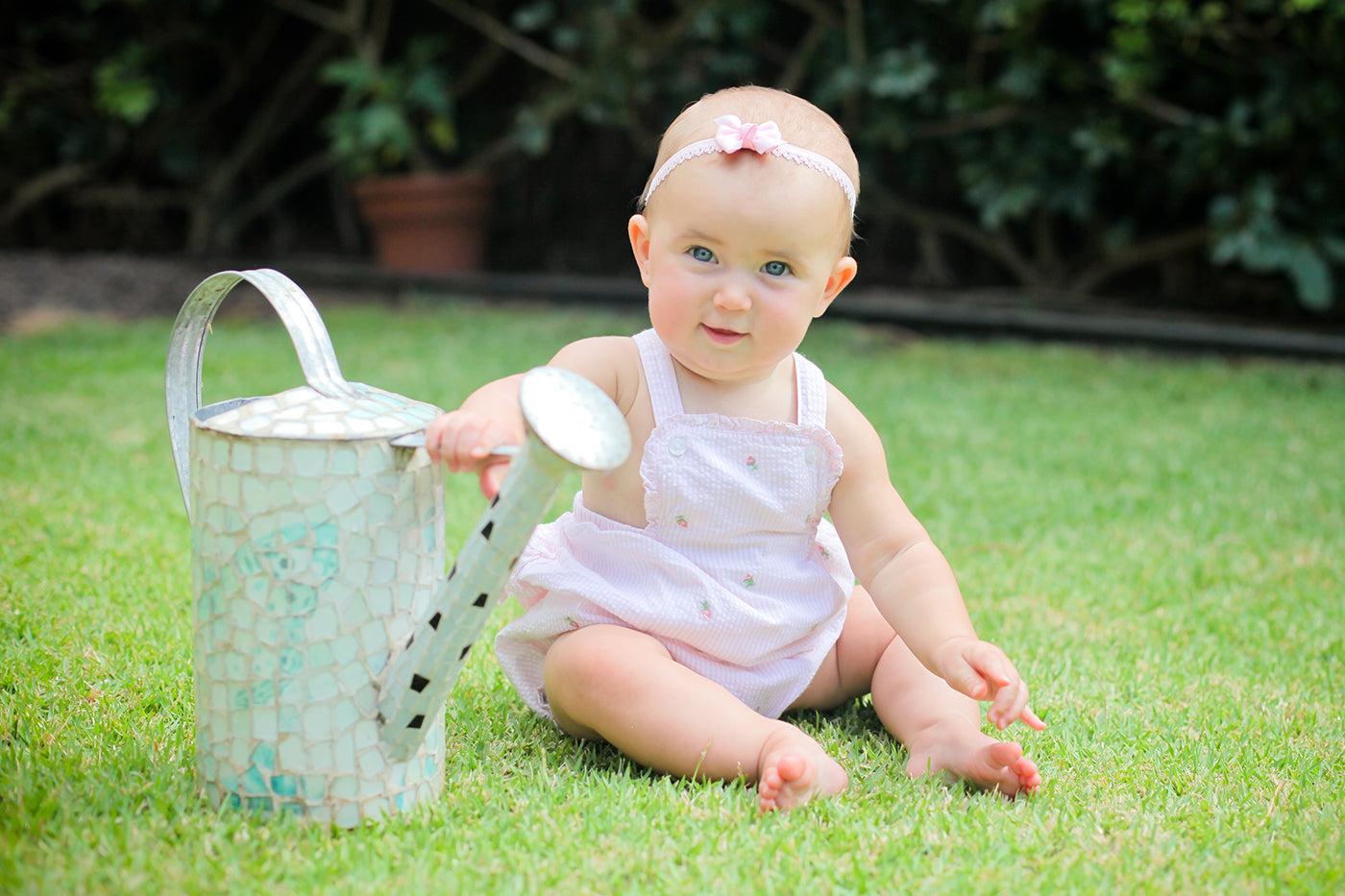 April baby facts: Cute baby girl sitting on the grass next to a watering can