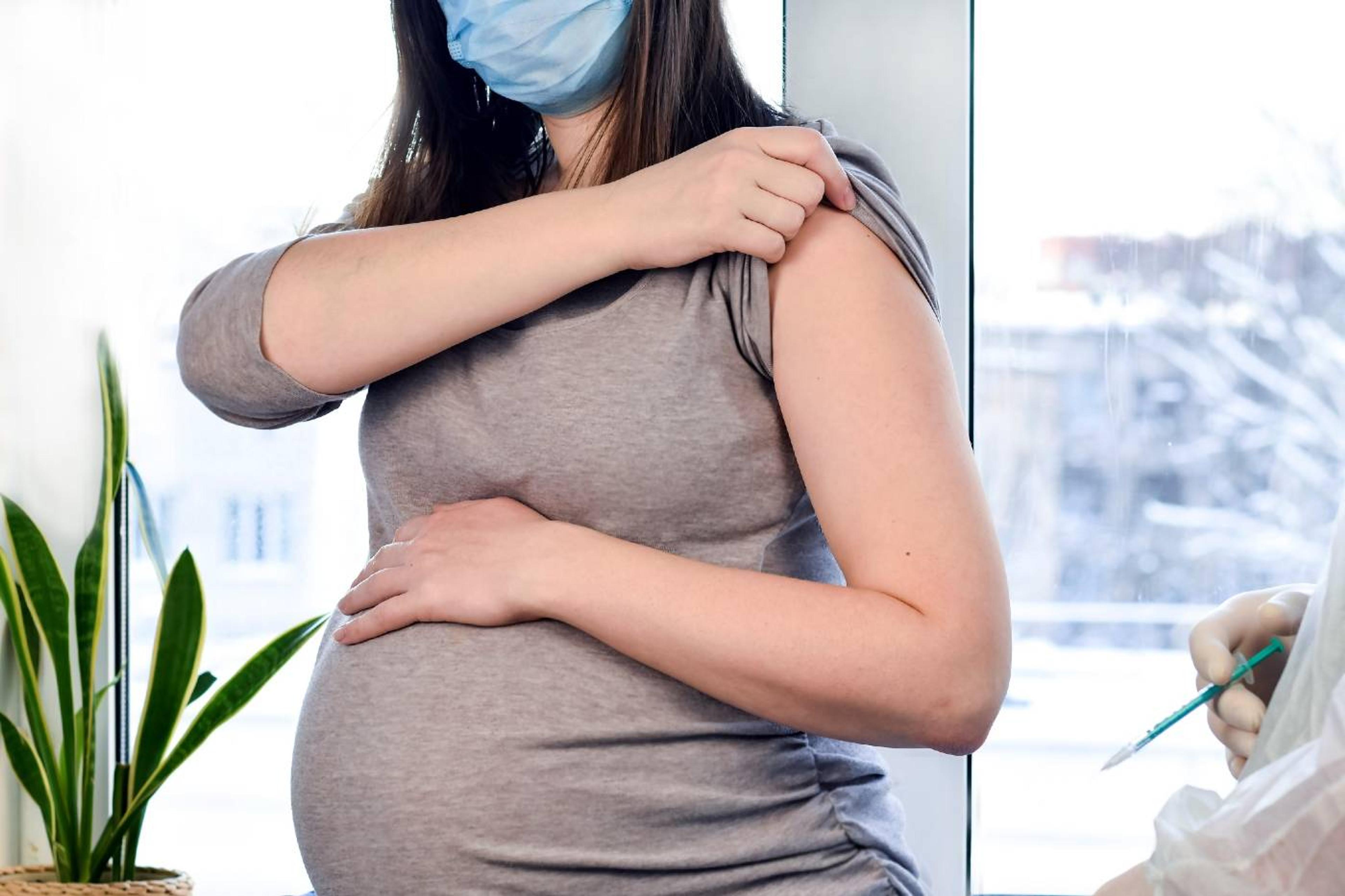 Masked pregnant person pulling sleeve up, ready for her COVID-19 vaccine 