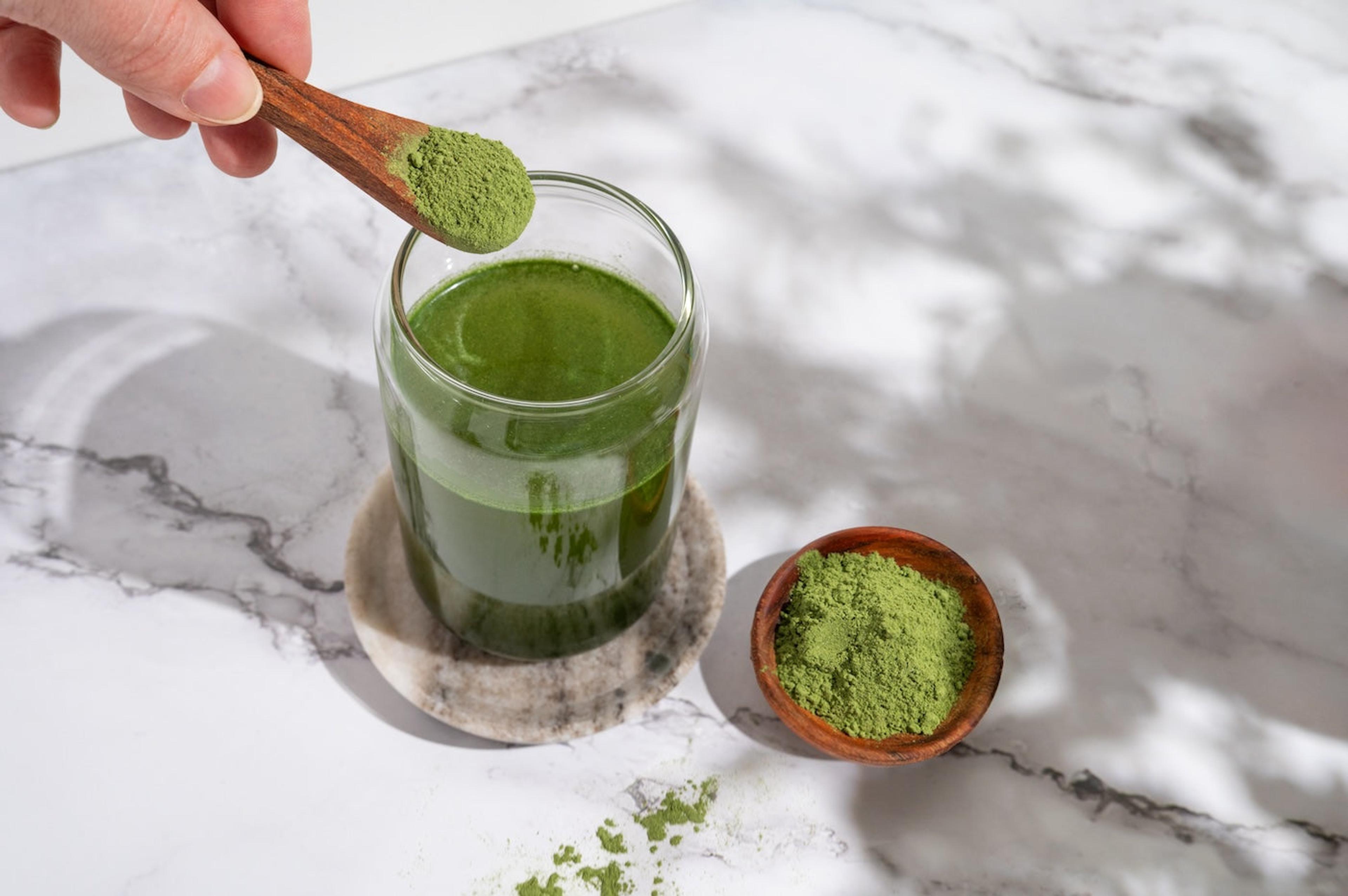 A woman adds barley grass powder to green juice