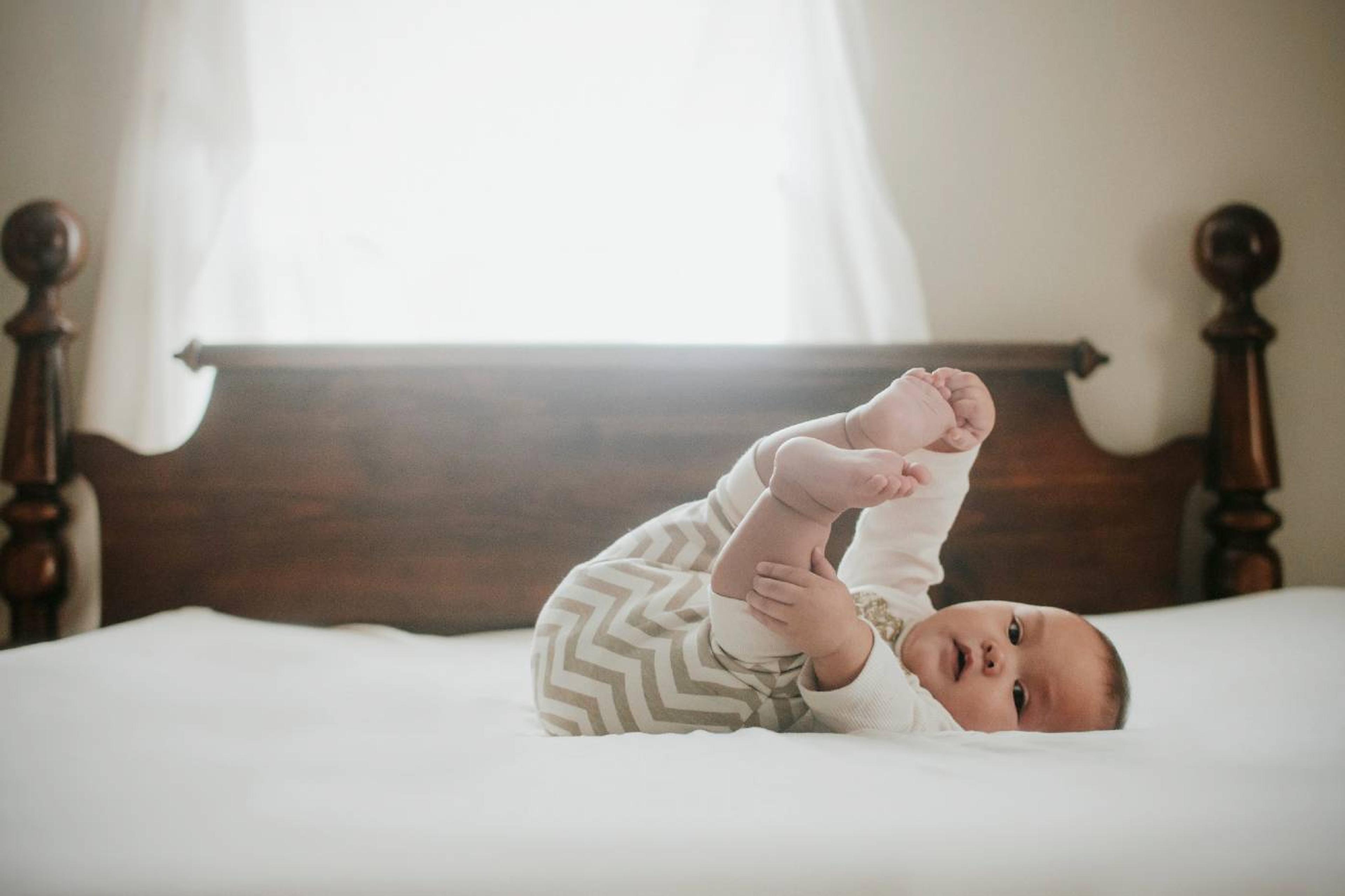 A baby lays on their back and grabs their toes
