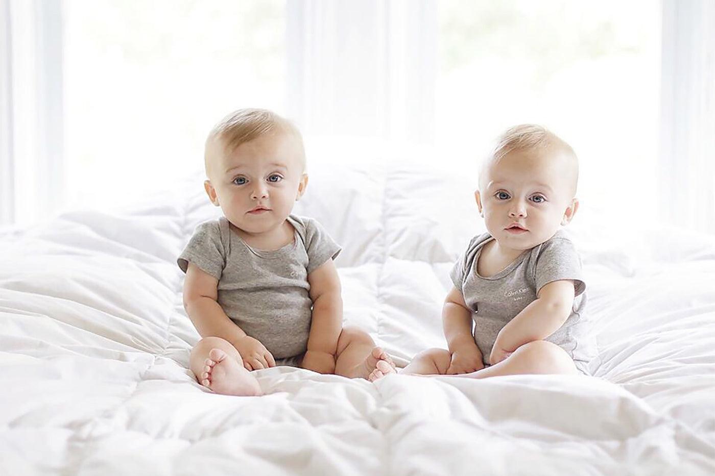 Twin babies sit on a bed