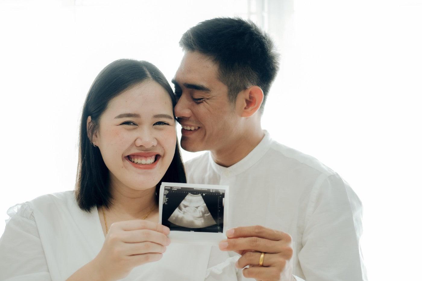 A couple holds up a baby ultrasound photo to announce a pregnancy