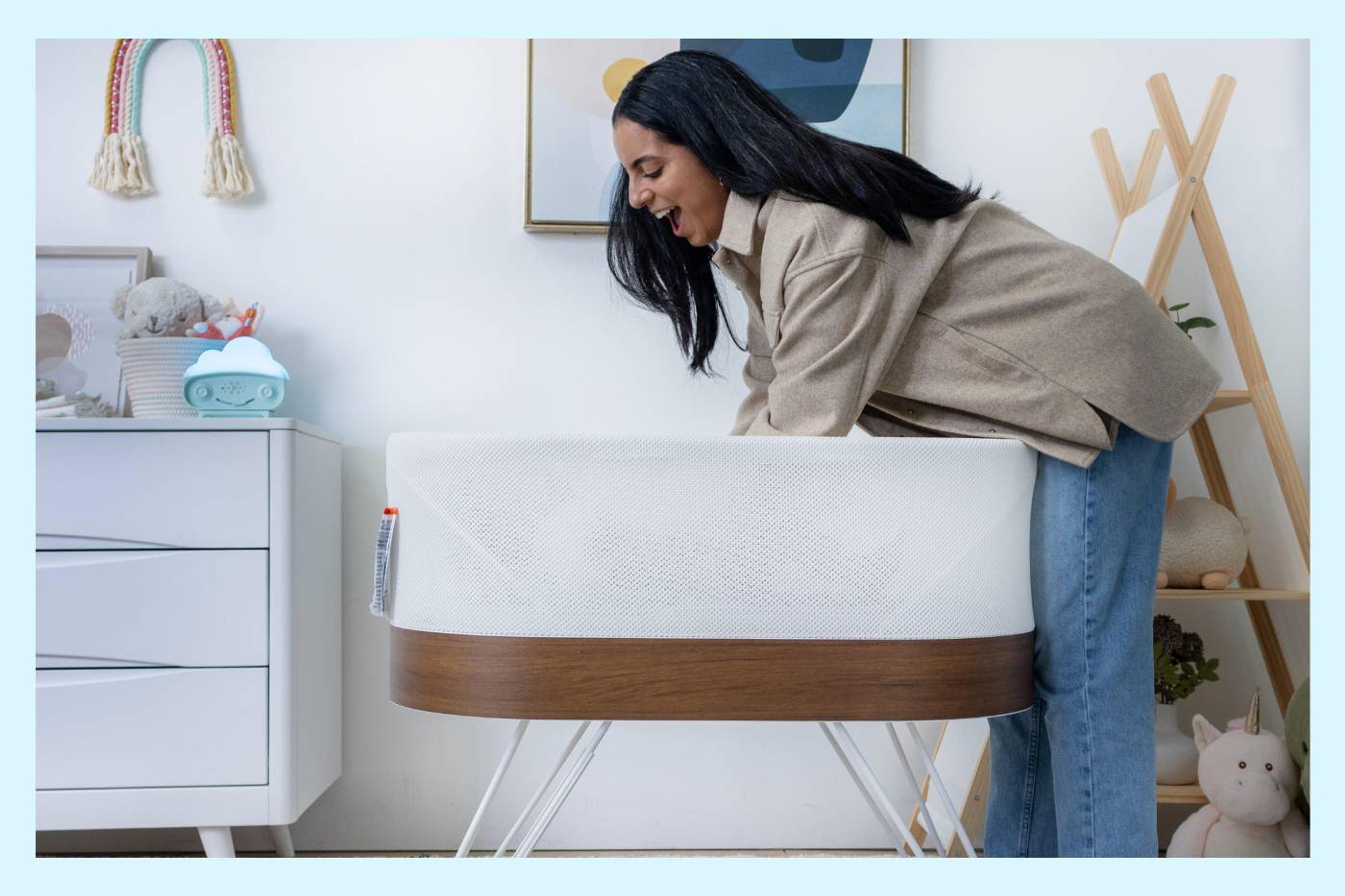 A mom leans over to put her baby in SNOO while smiling