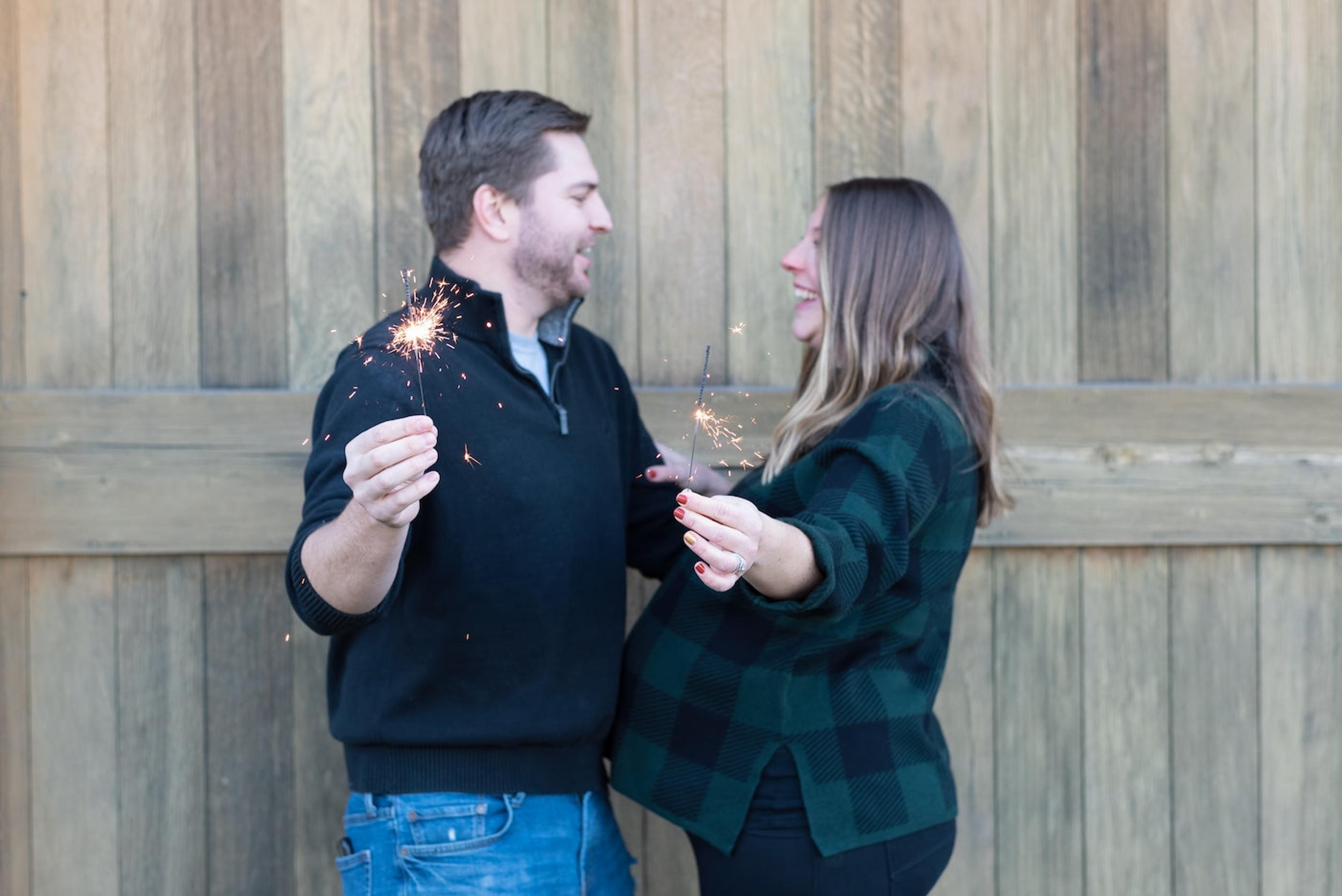 A pregnant woman and her partner hold sparklers in a 4th of July pregnancy announcement