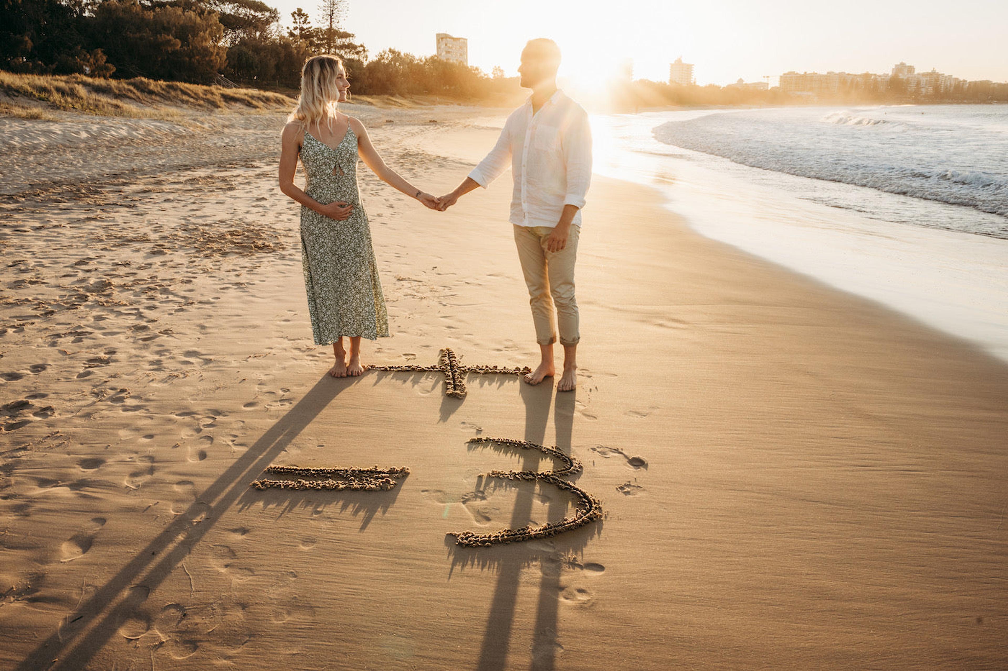 A couple poses on the beach to announce a pregnancy