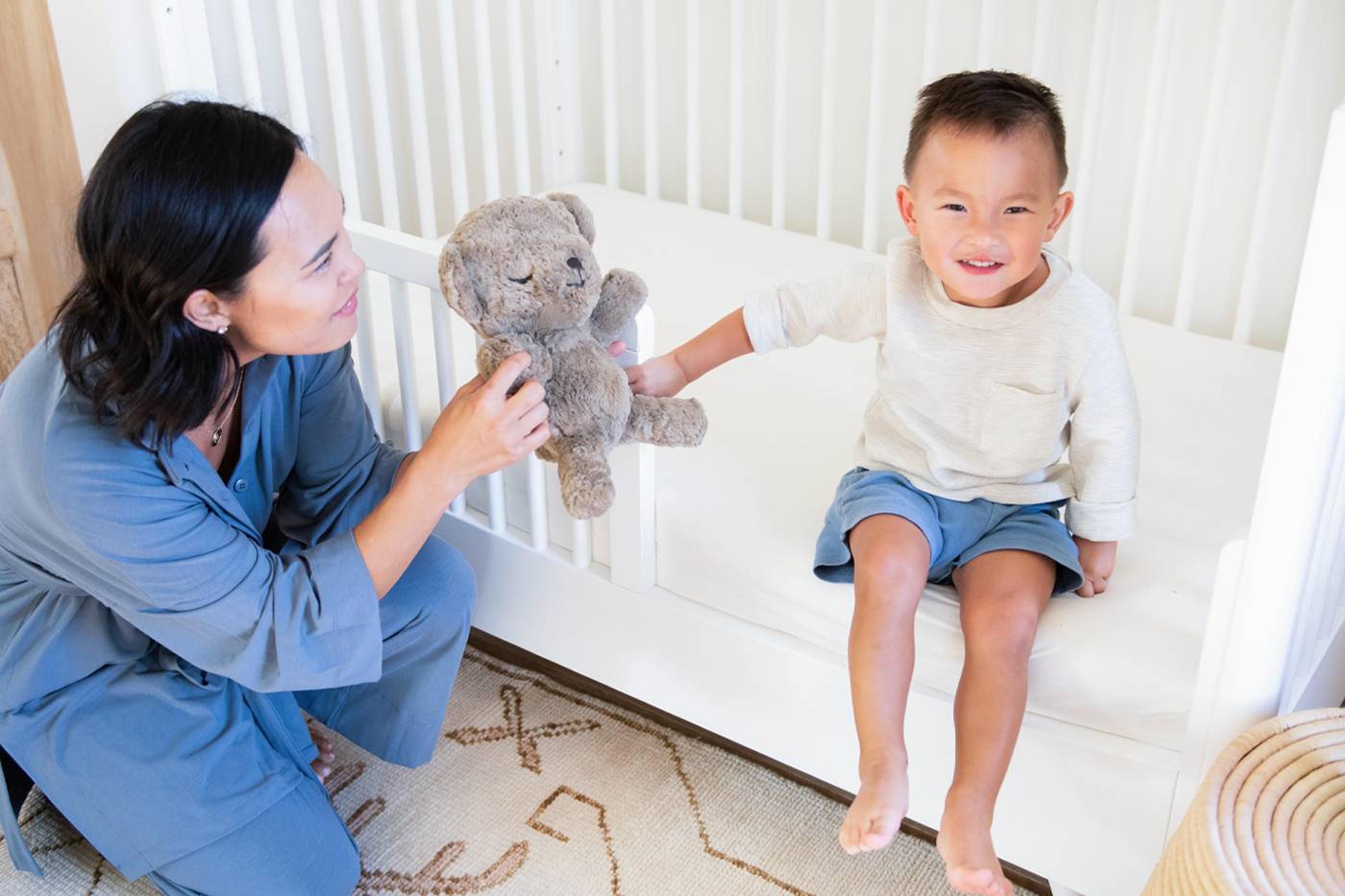 Happy toddler sitting in Lola toddler bed, with mom and SNOObear