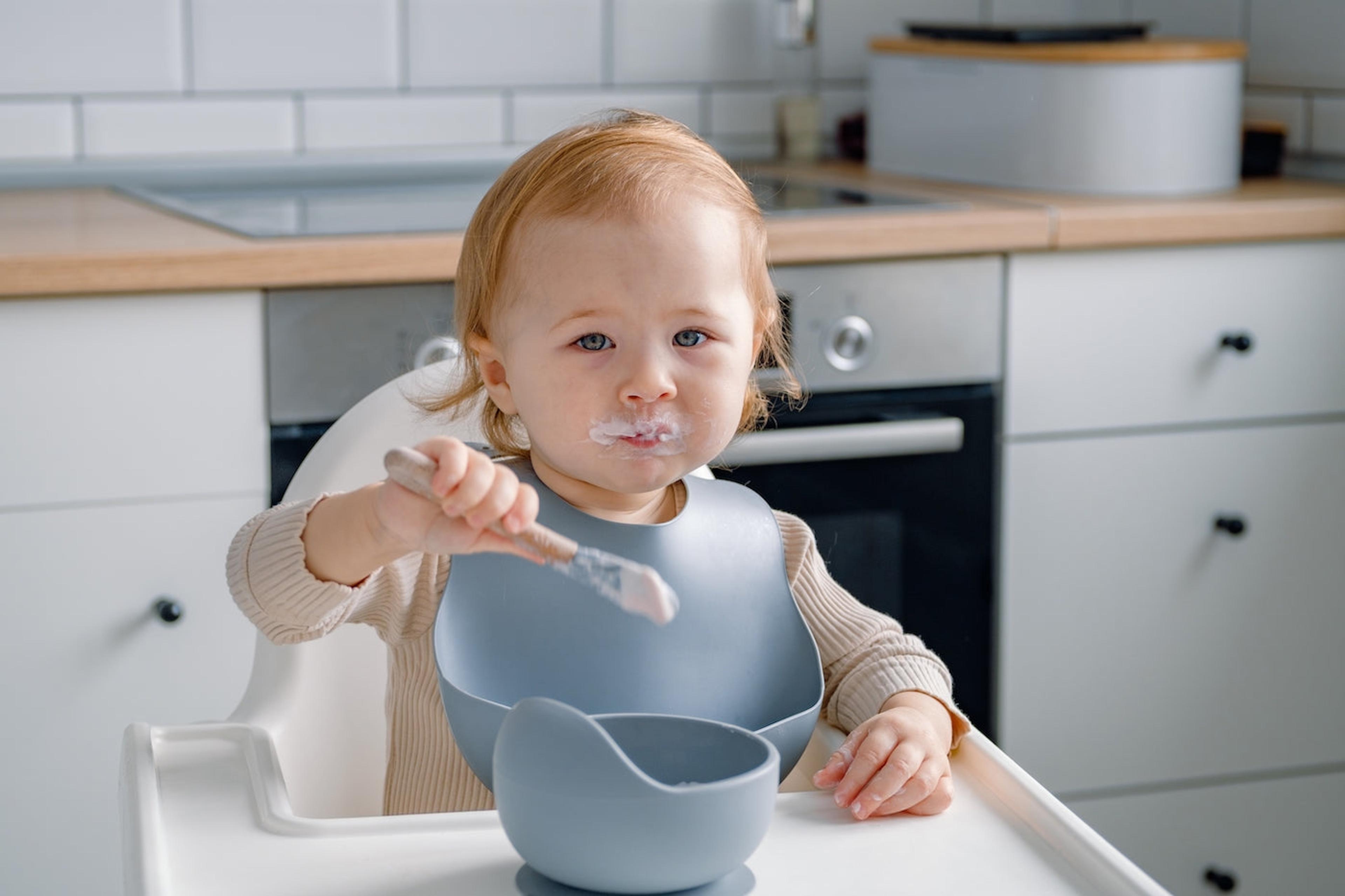 A baby eats calcium-rich yogurt in a highchair
