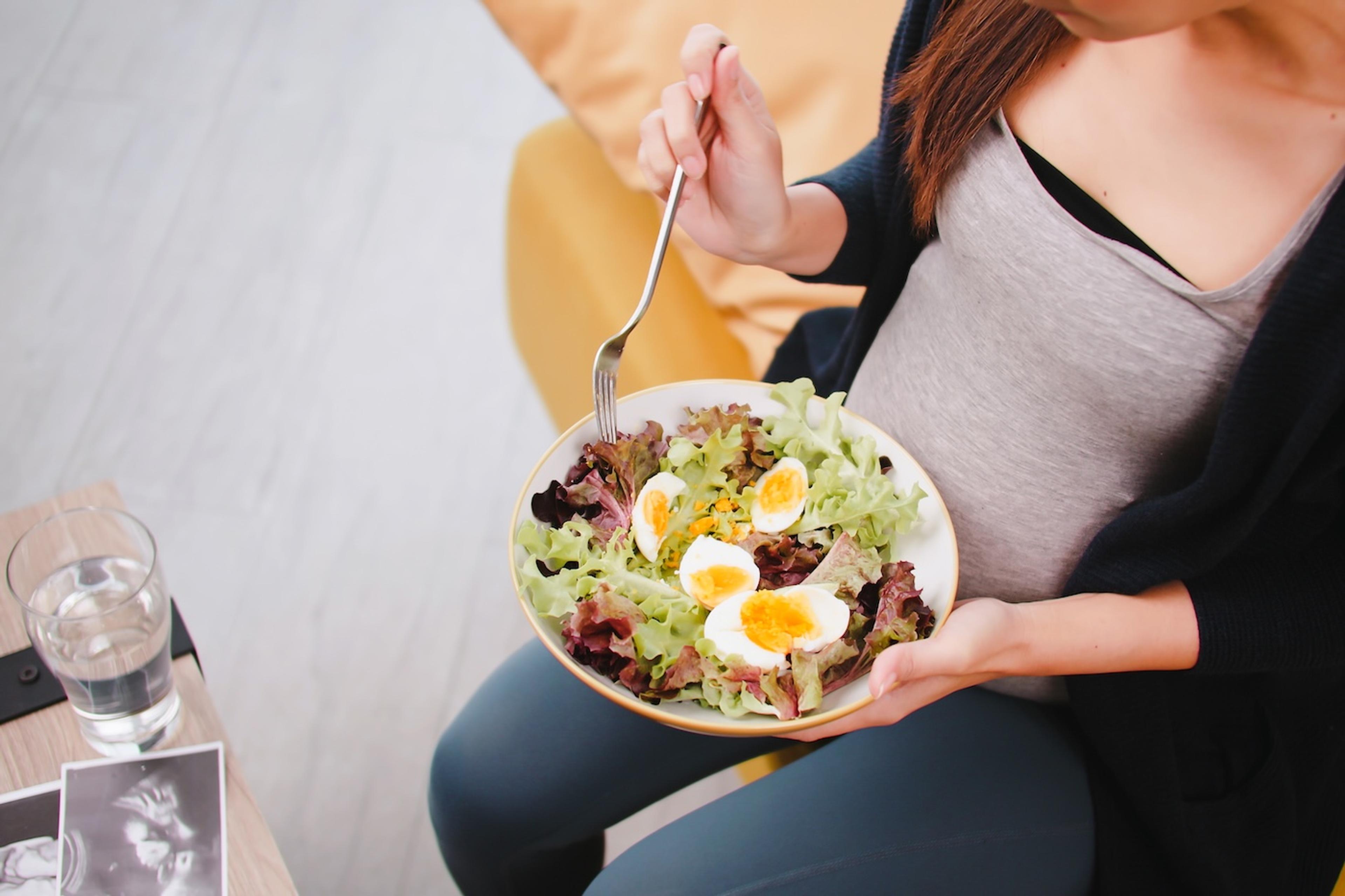 A pregnant woman eats hard boiled eggs on a salad