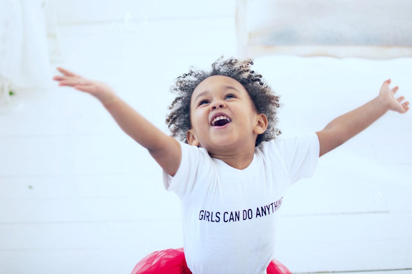 A happy little girl wearing a shirt that says "girls can do anything"