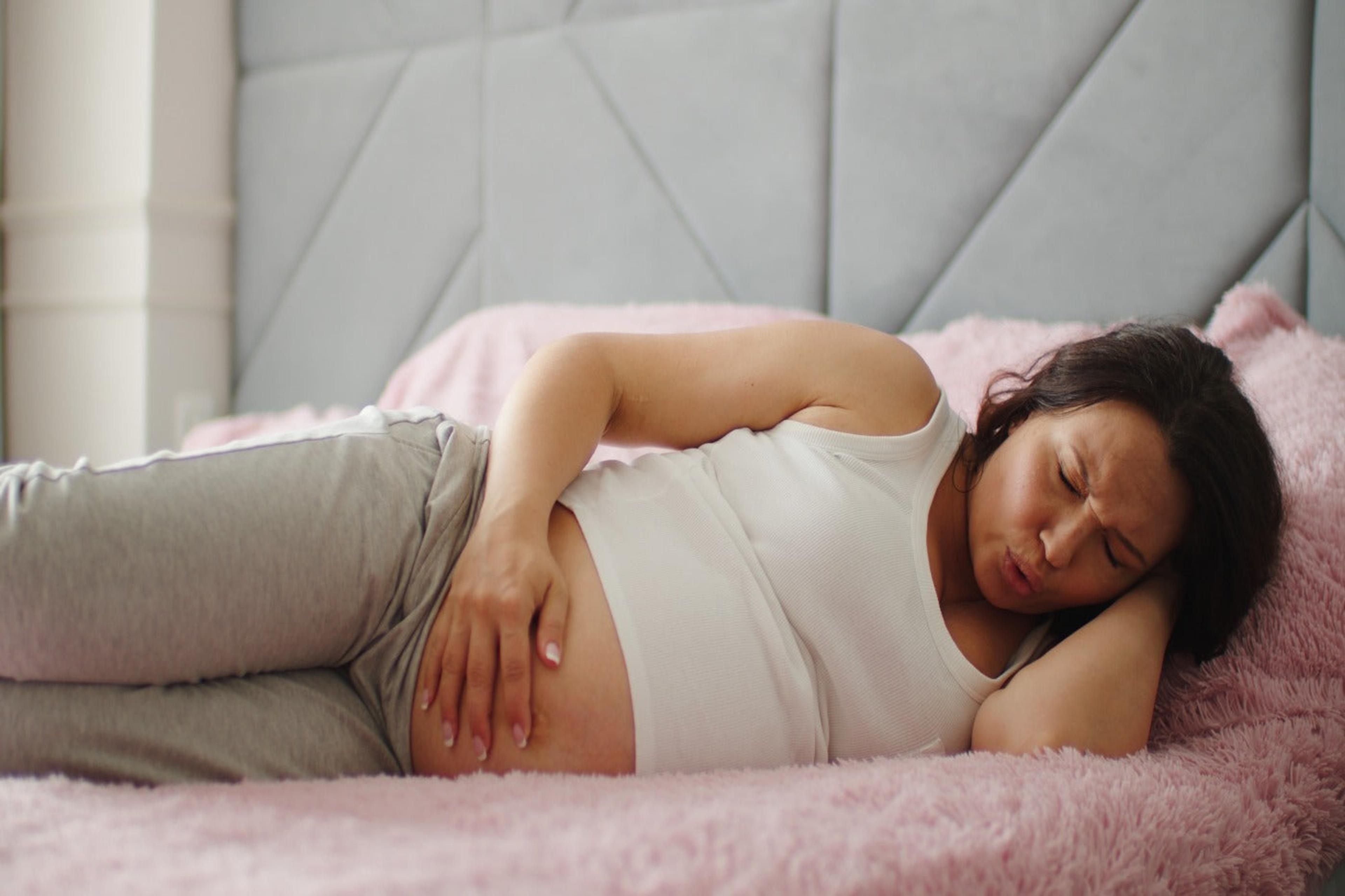Woman on bed experiencing round ligament pain in pregnancy