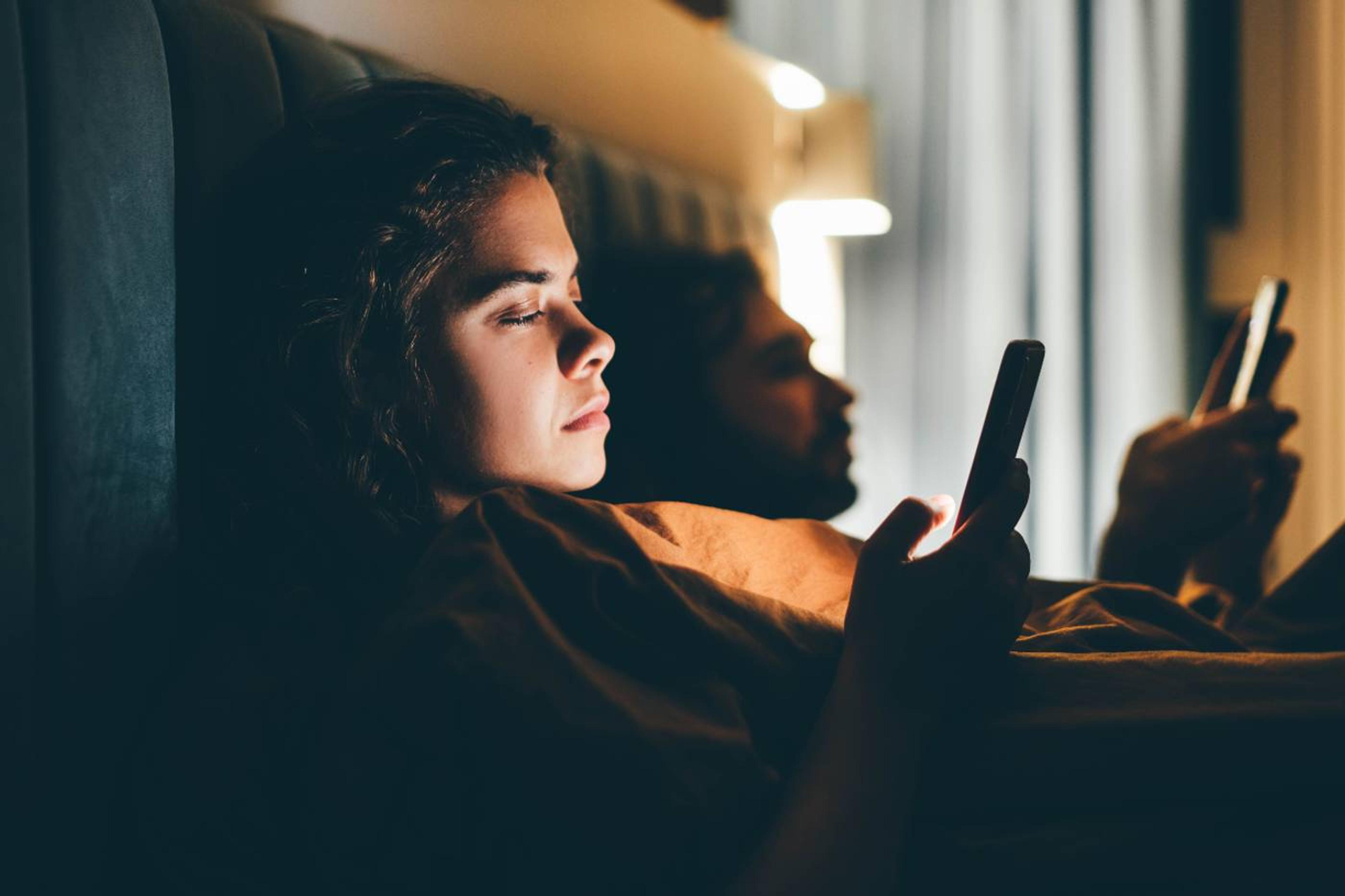 couple in bed on phones engaging in revenge bedtime procrastination 