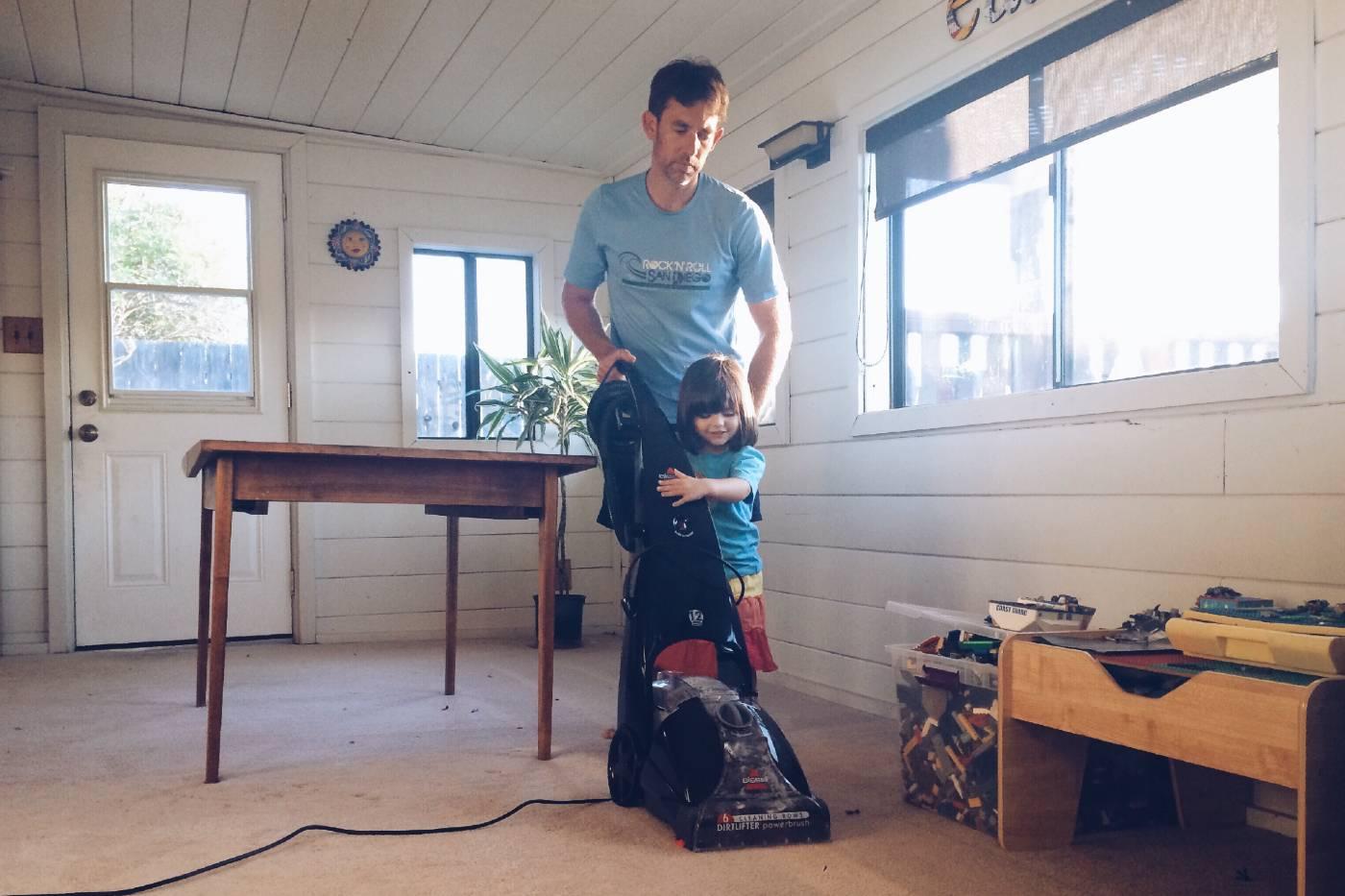 Dad and toddler daughter vacuuming together