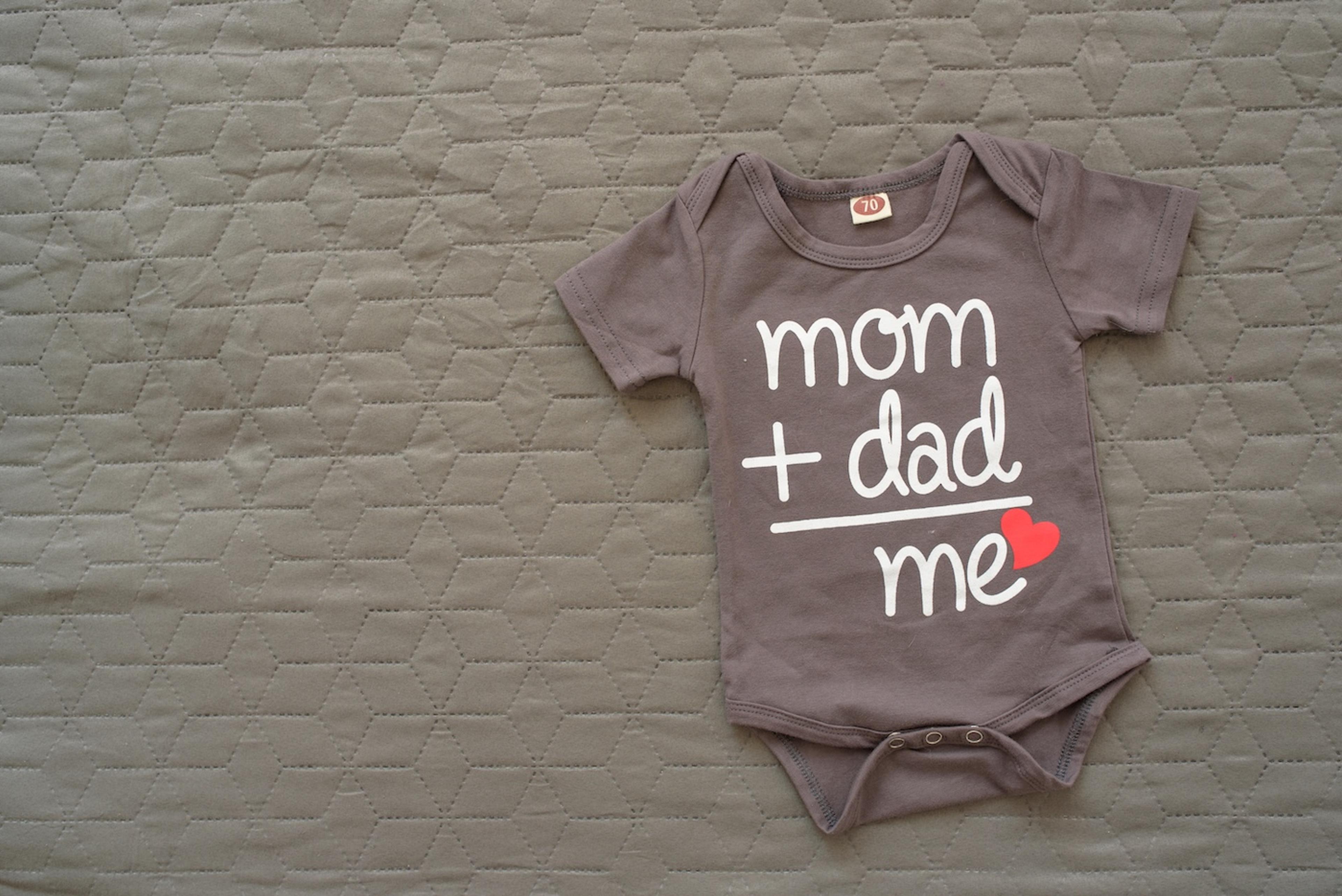 Pregnancy announcement onesie that reads "mom + dad = me"