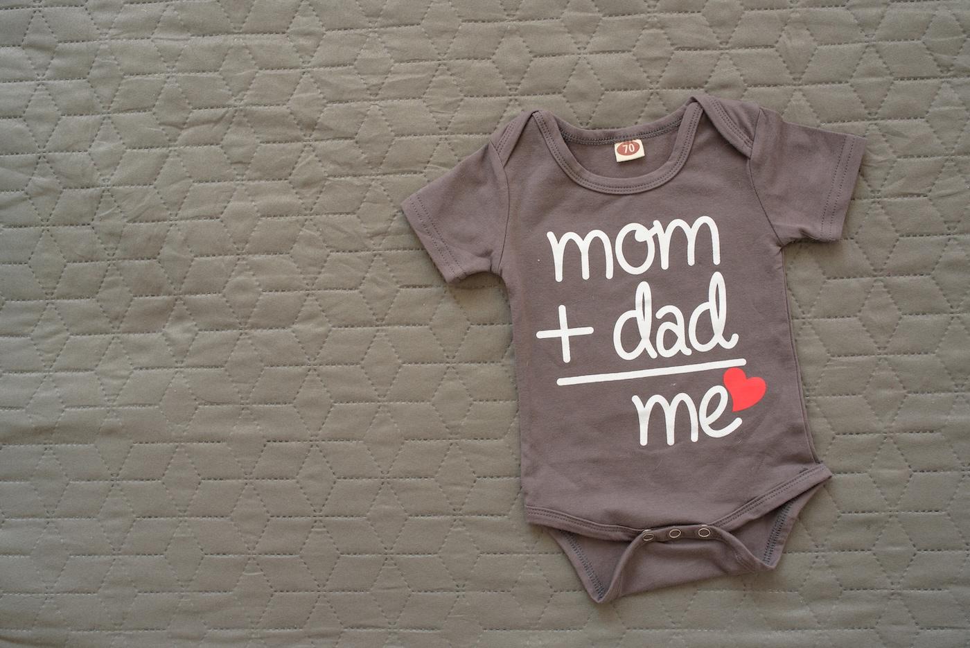 Pregnancy announcement onesie that reads "mom + dad = me"