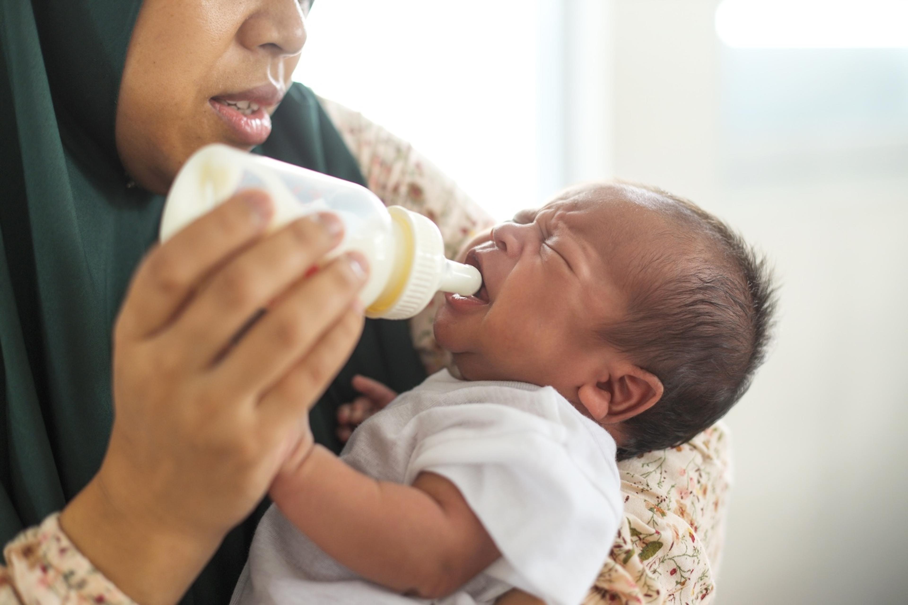 A fussy baby refuses a bottle from their mother