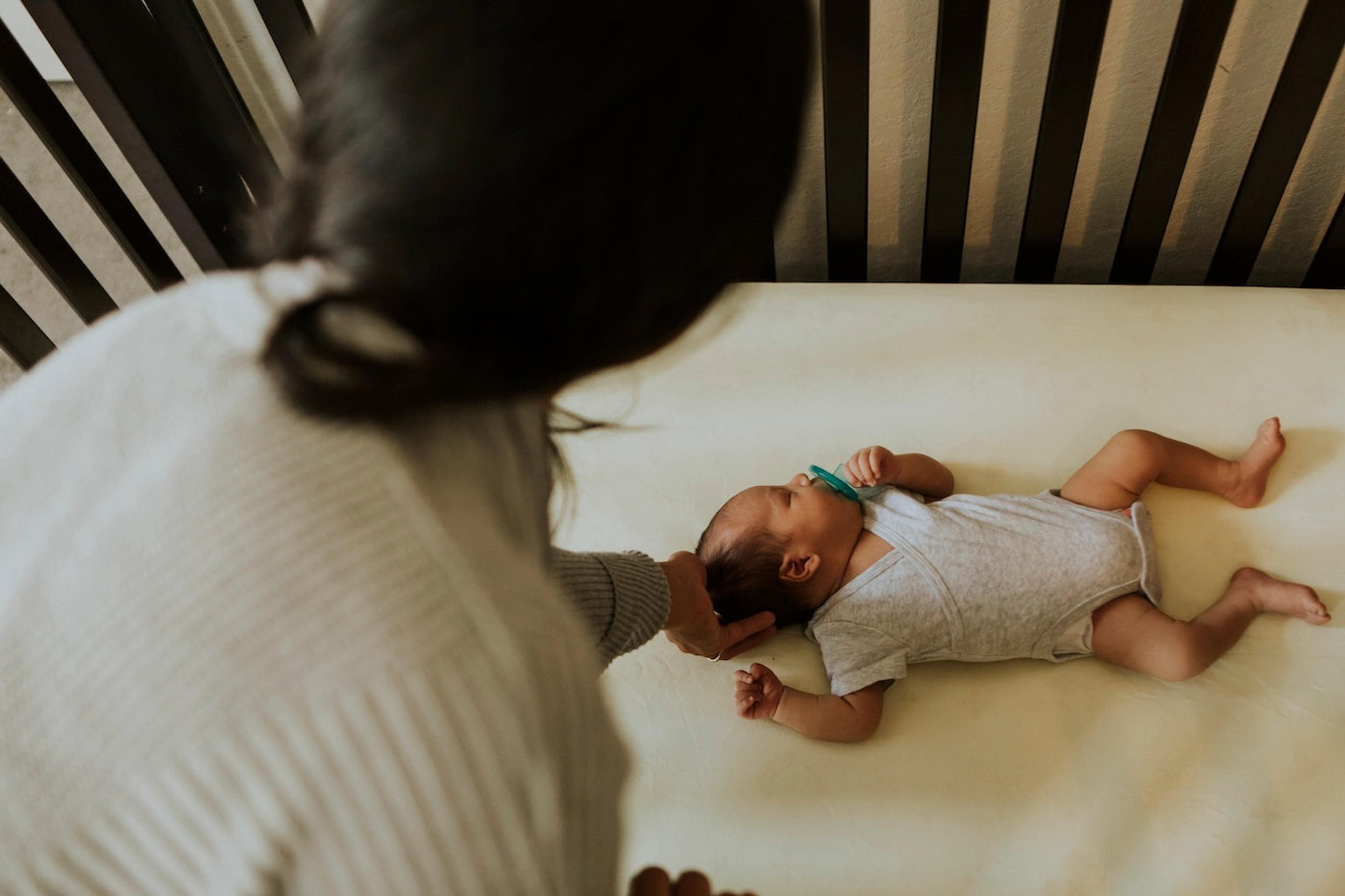 Mother tending to a baby sleeping on their back in a crib
