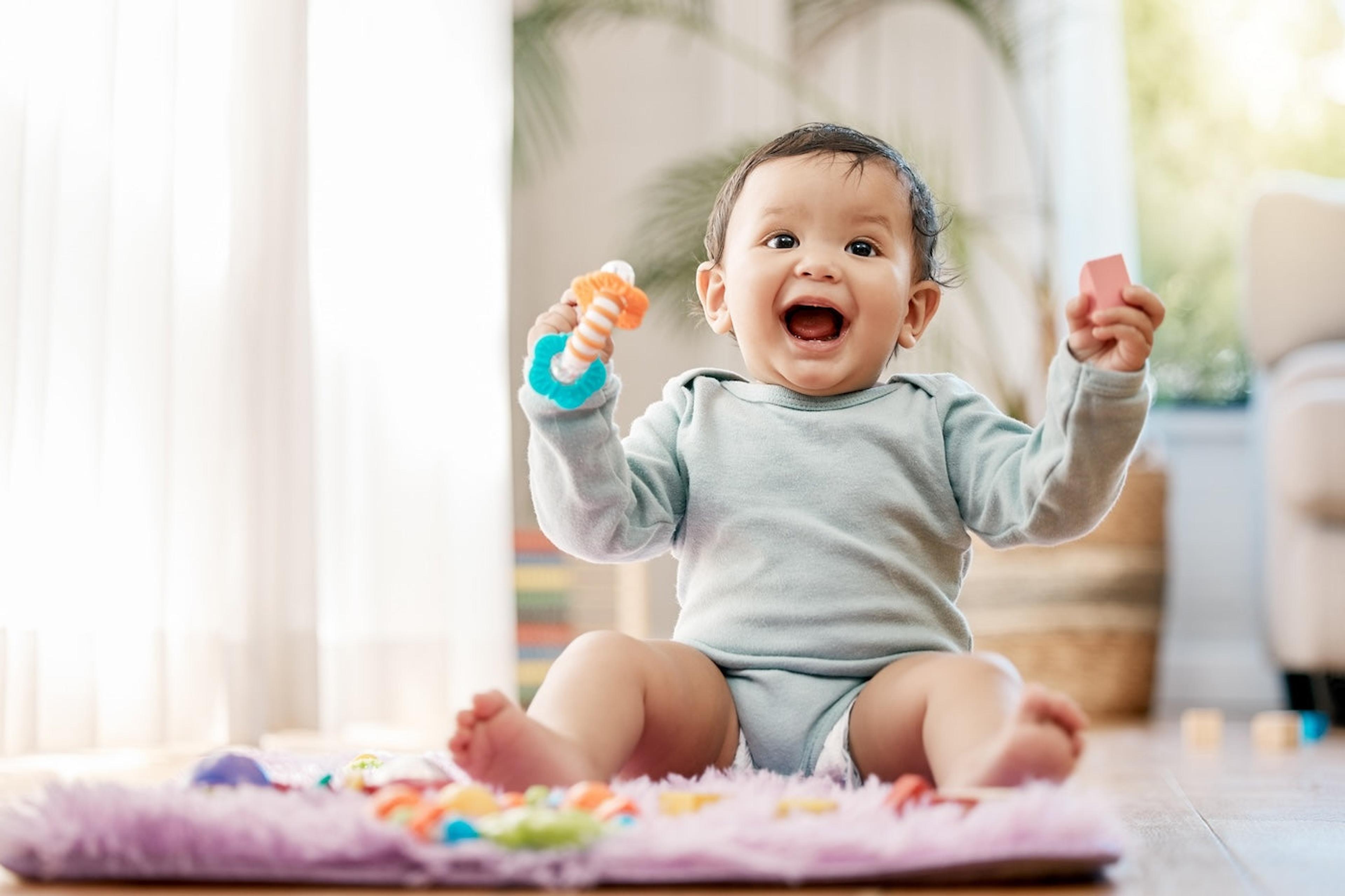 An excited baby sitting up and holding a toy