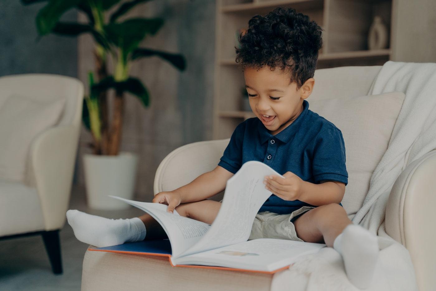 A 3-year-old boy smiles as he reads a book