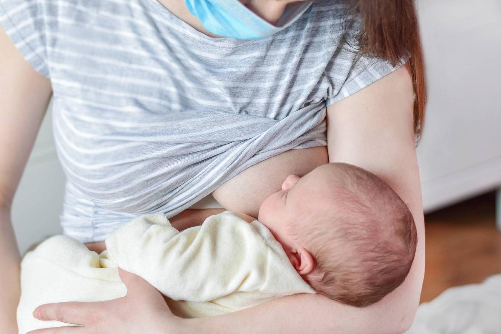 Masked mom with a cold breastfeeds baby