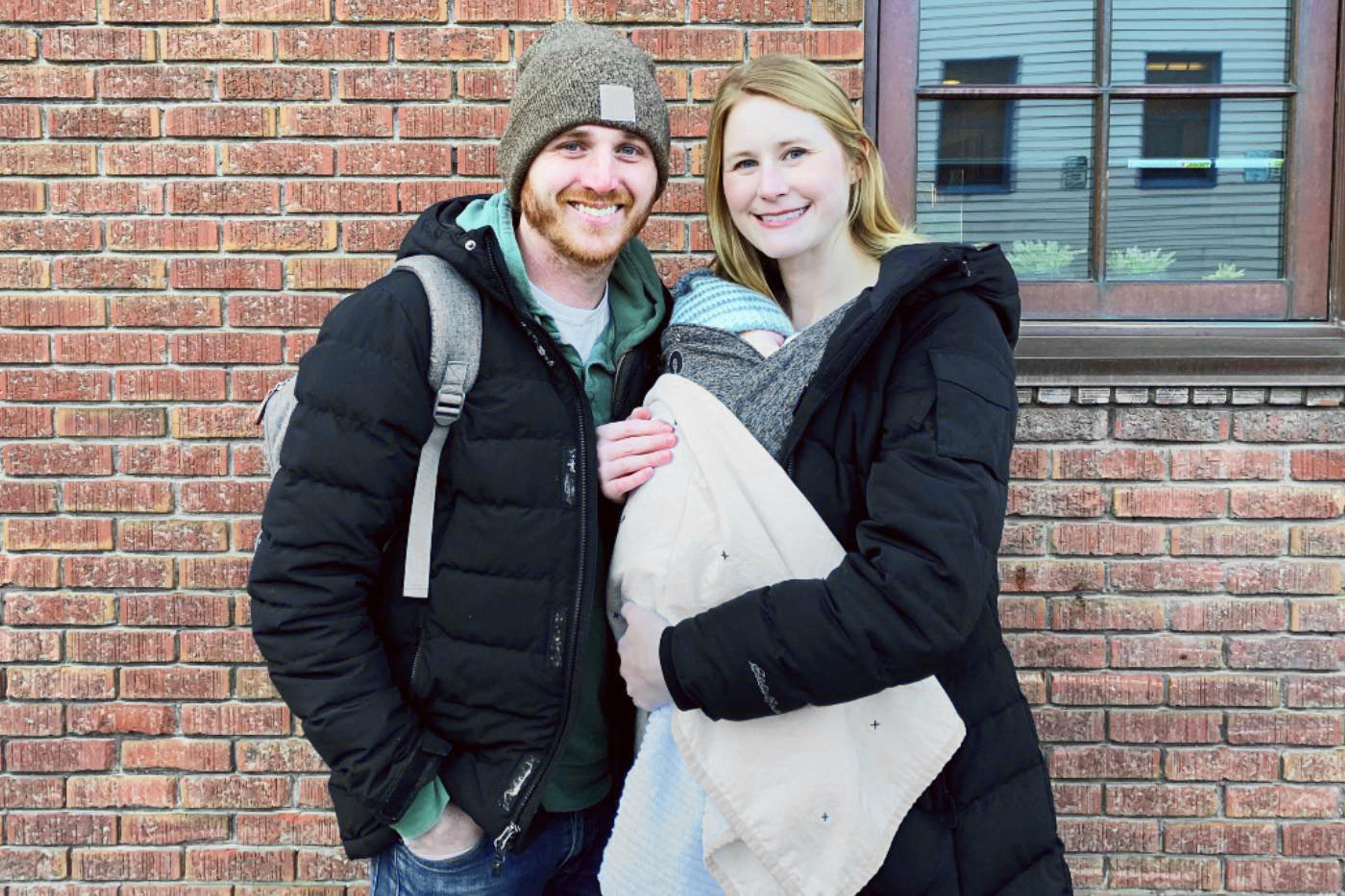 Smiling mom and dad outside, holding their new baby