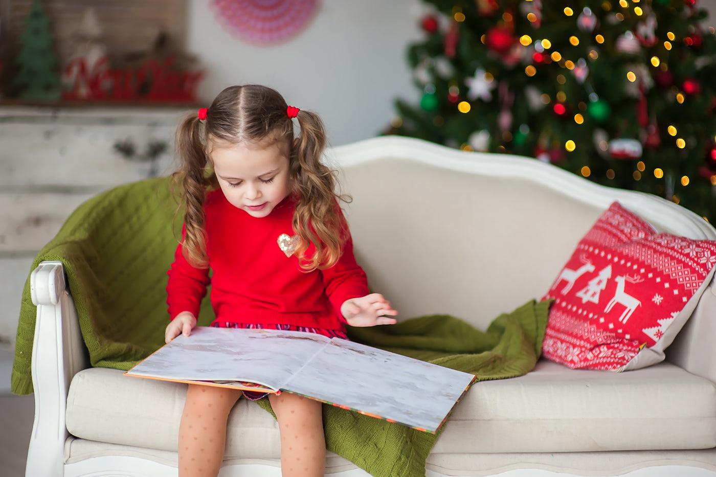 holiday books for kids: Child reading book near a Christmas tree