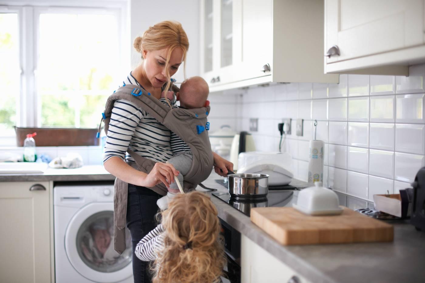 mom juggling two kids in the kitchen, carrying the mental load of parenting