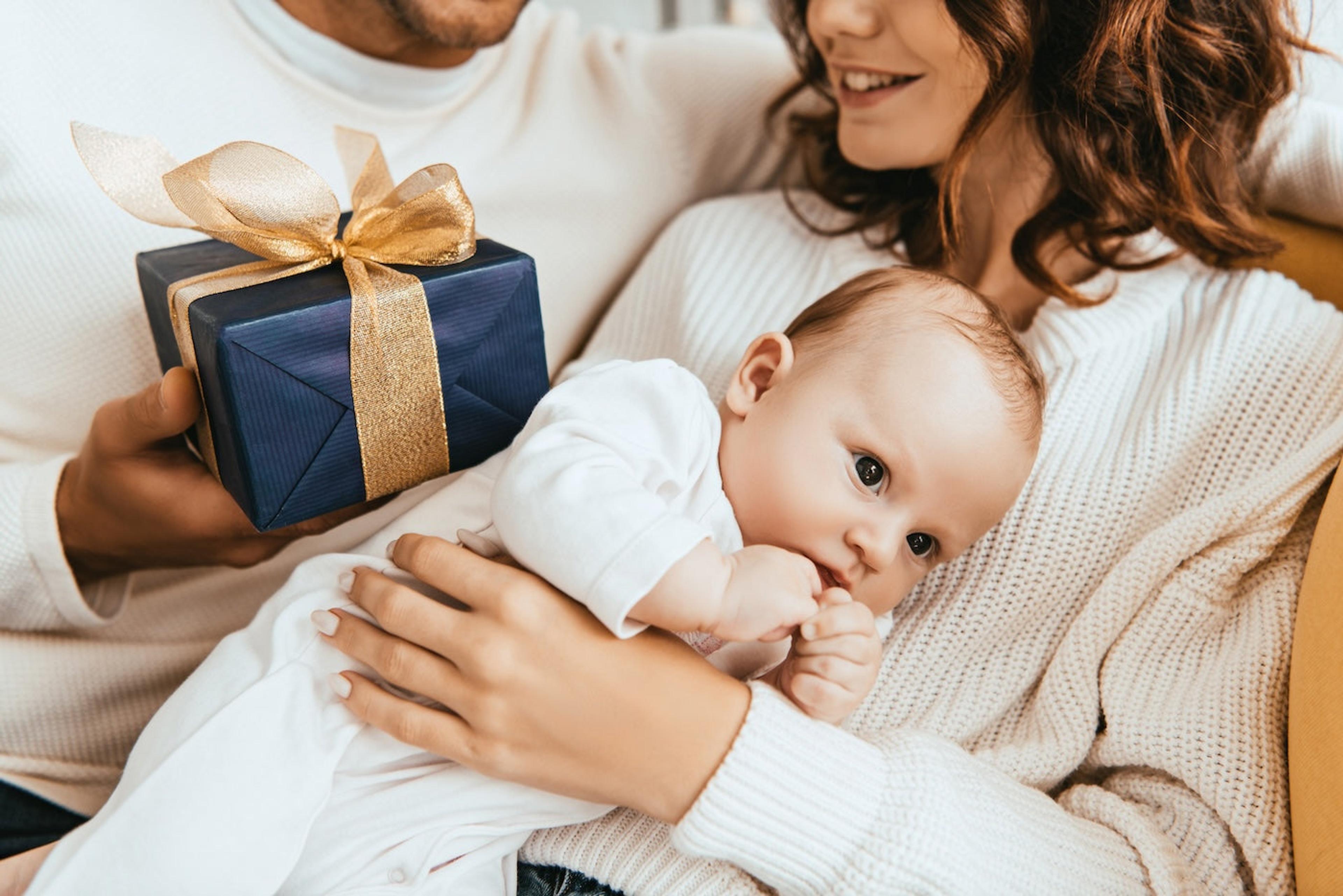 A dad presents a new mom with a wrapped push present as she holds her baby