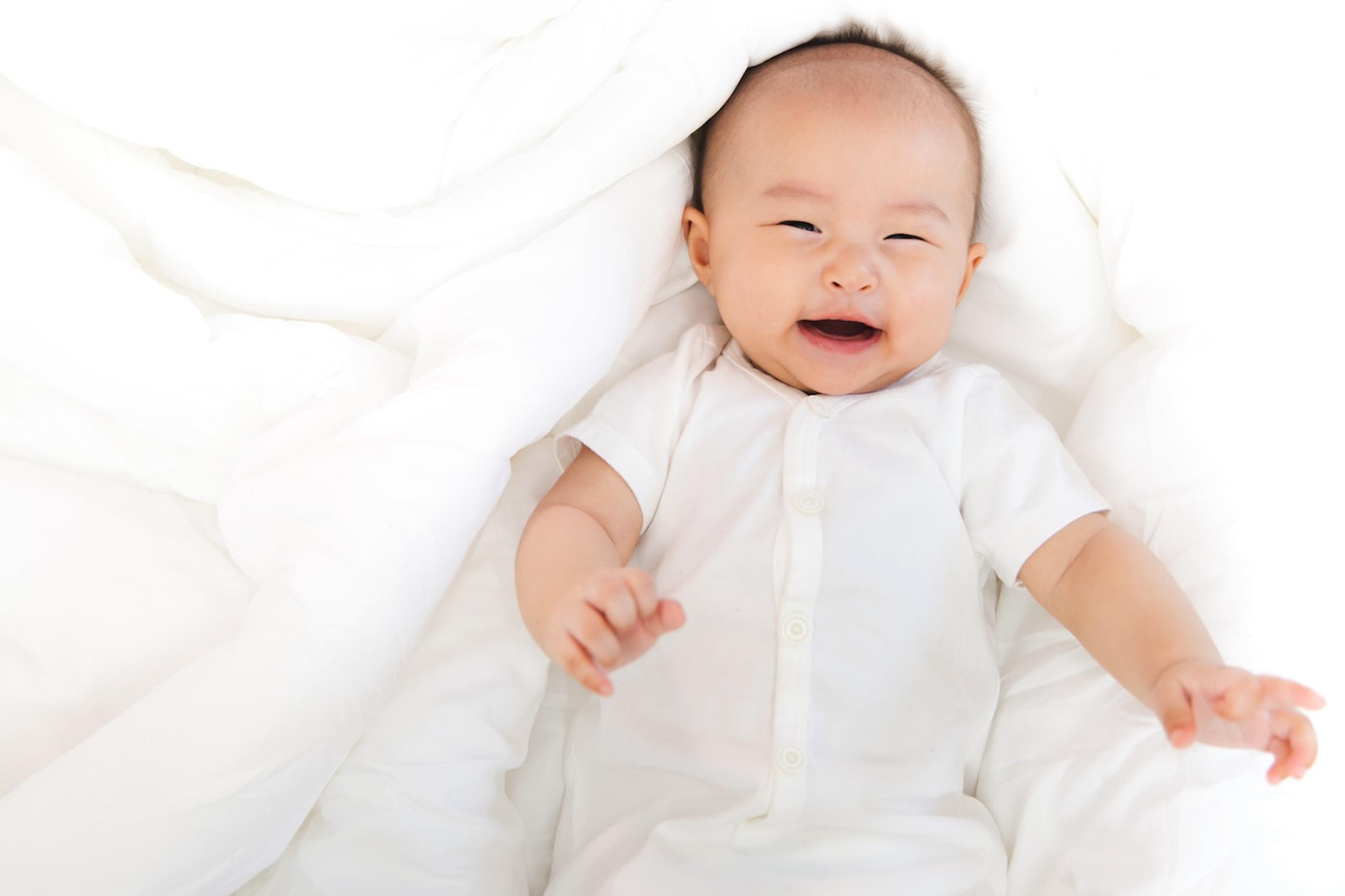 Happy baby dressed in white laying on white blankets