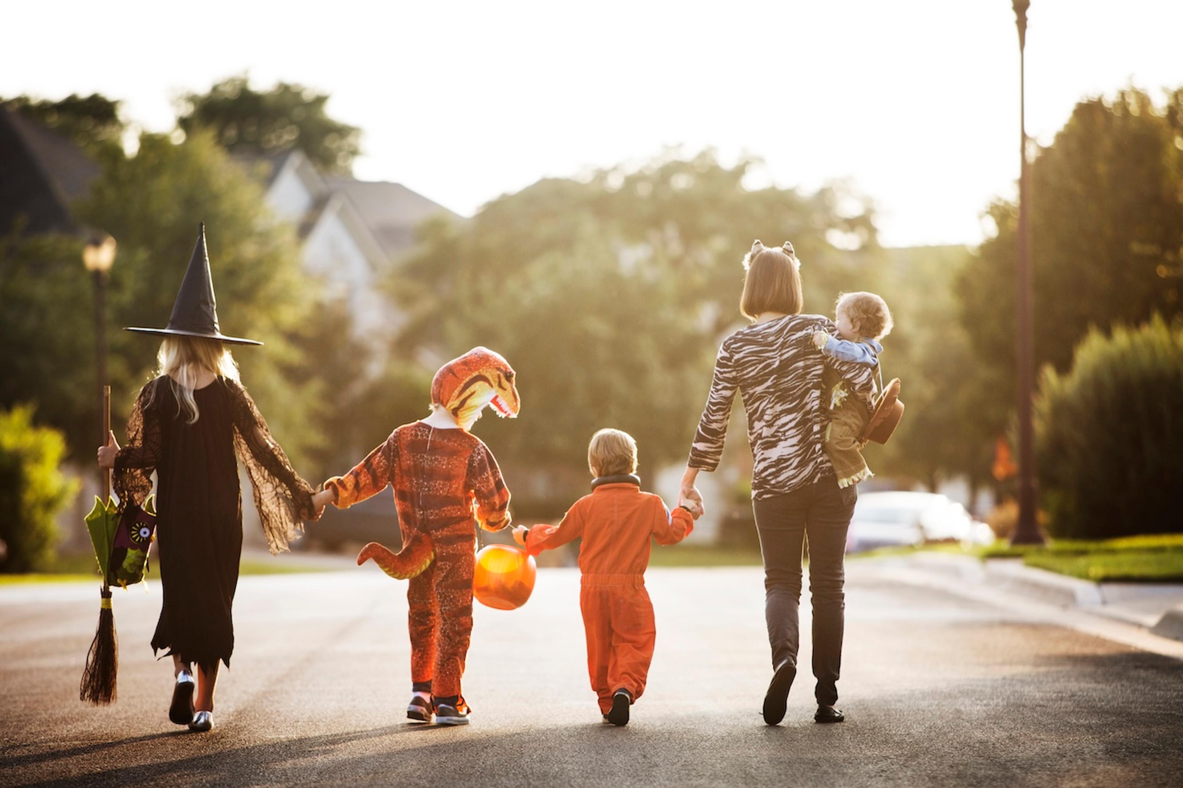 A family in costume walks down an empty suburban street during the day on Halloween