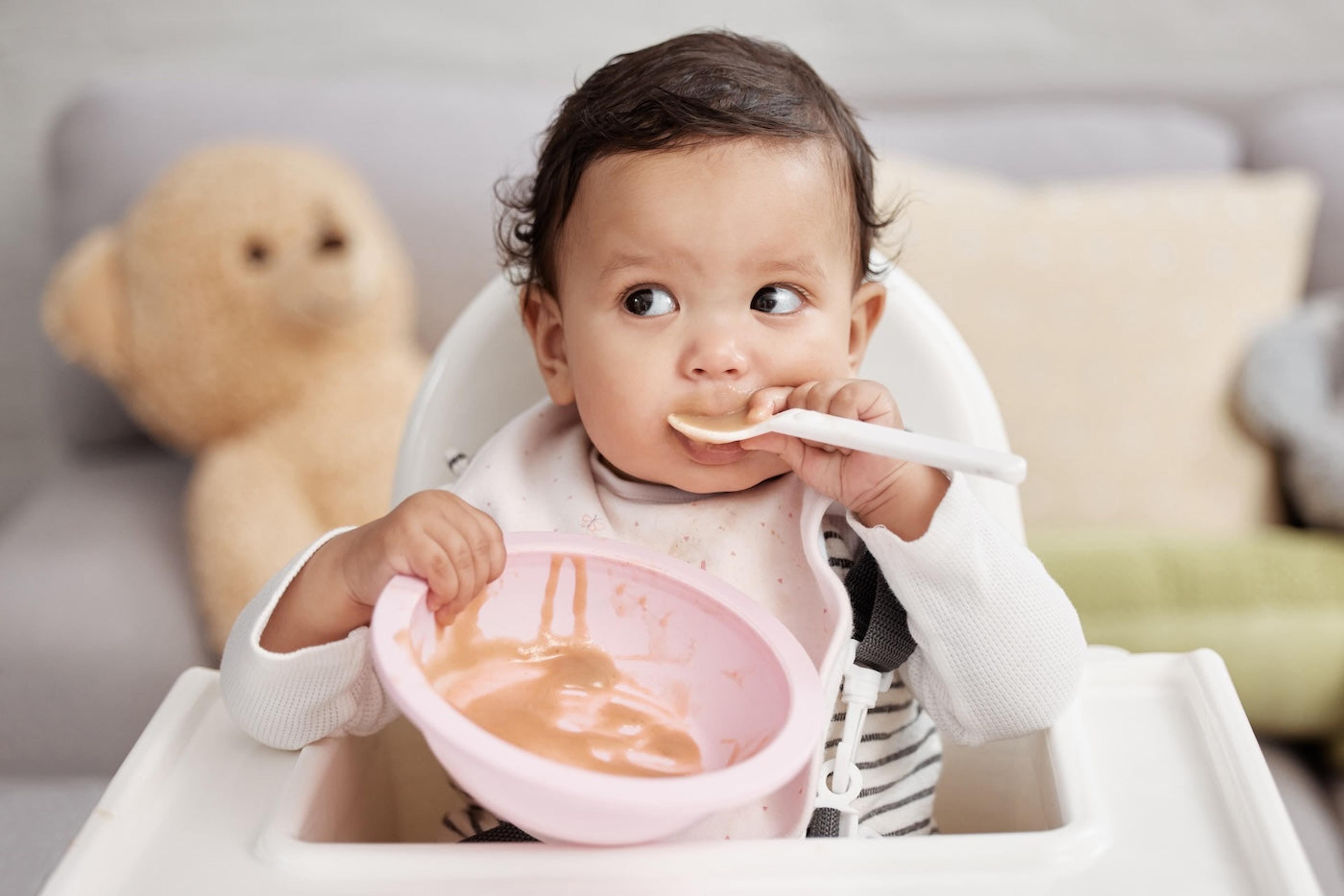 Baby feeds self with spoon in highchair