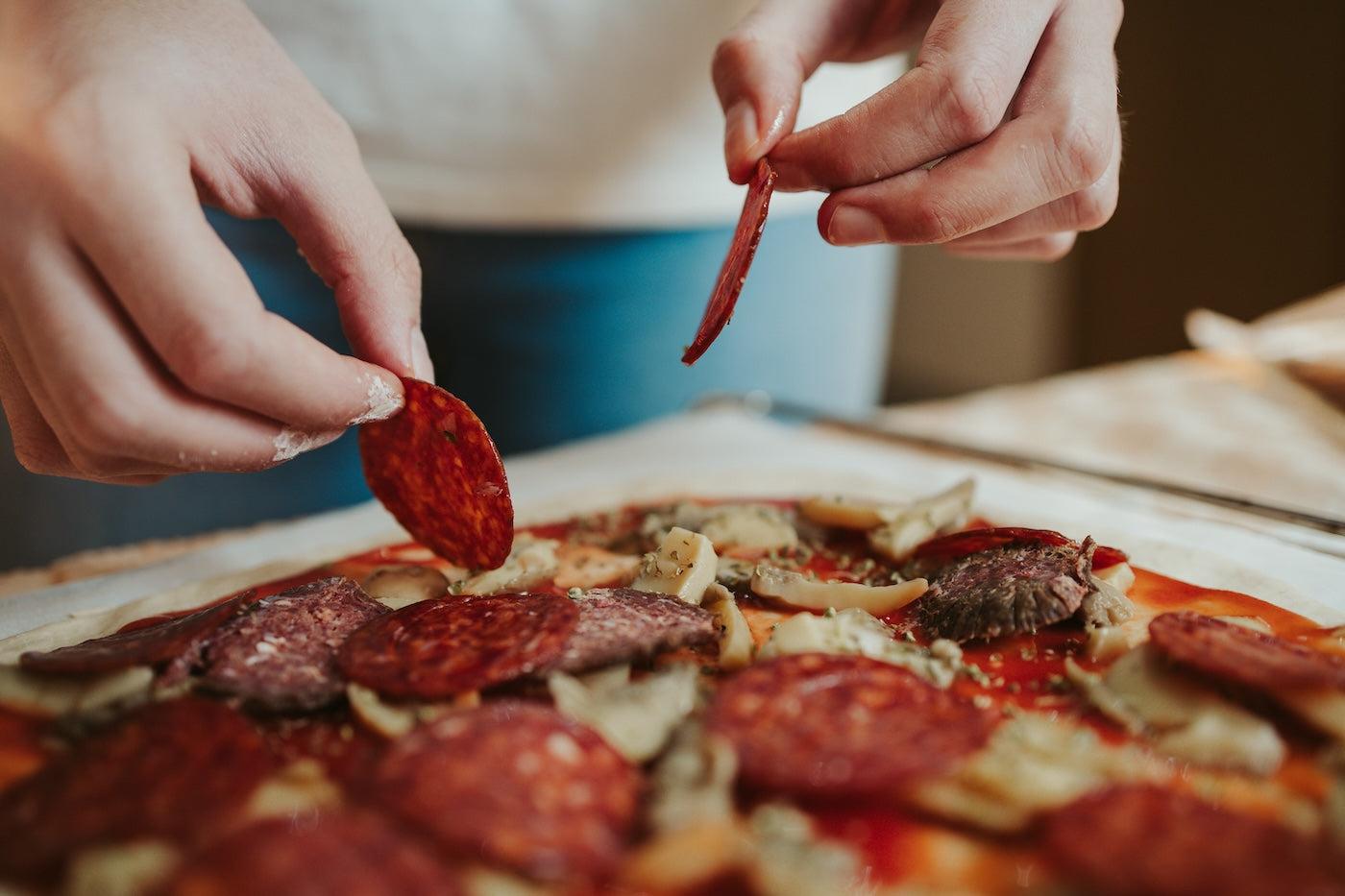 A woman puts pepperoni on a pizza