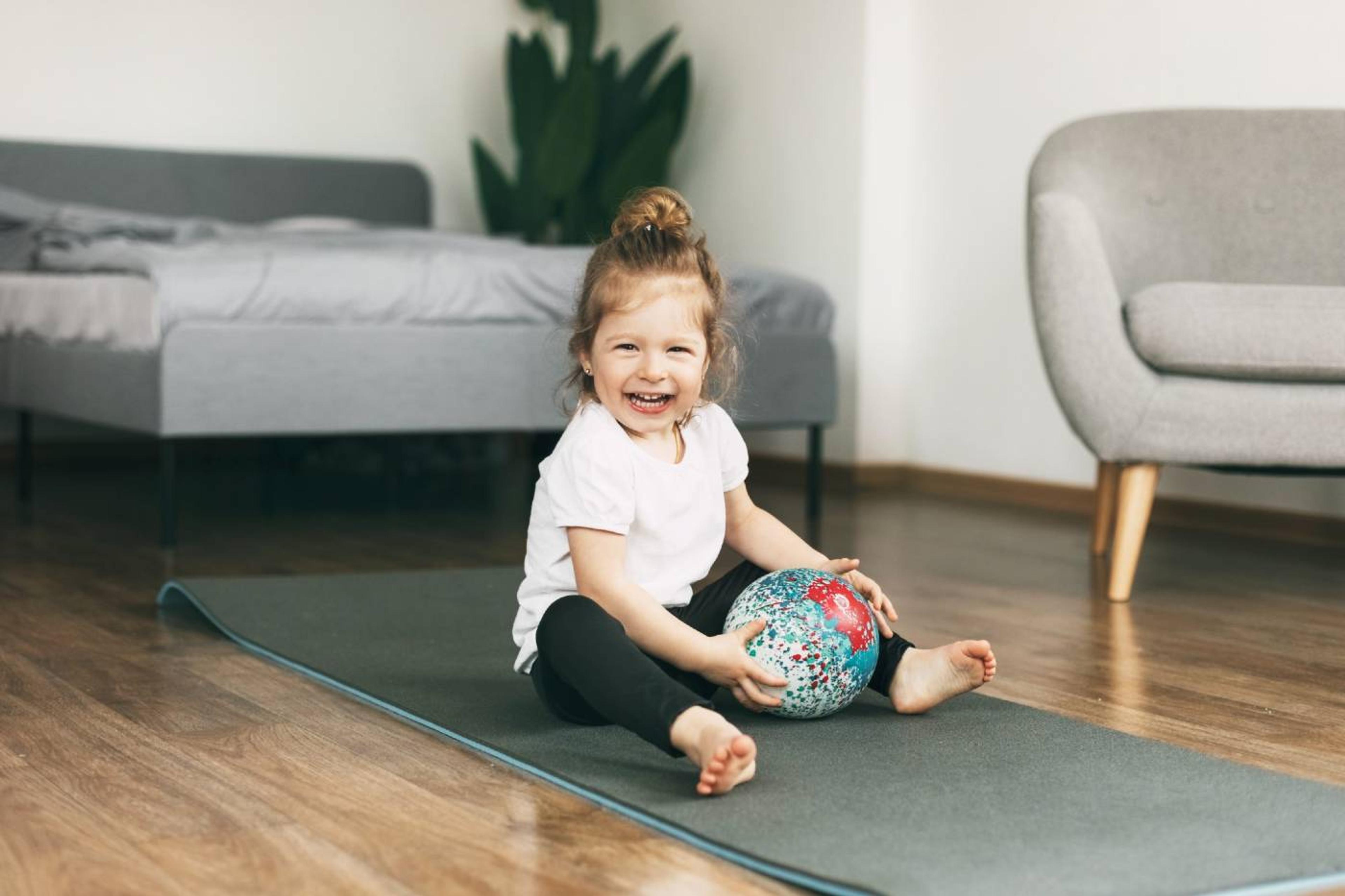A toddler girl plays with a ball on the floor.