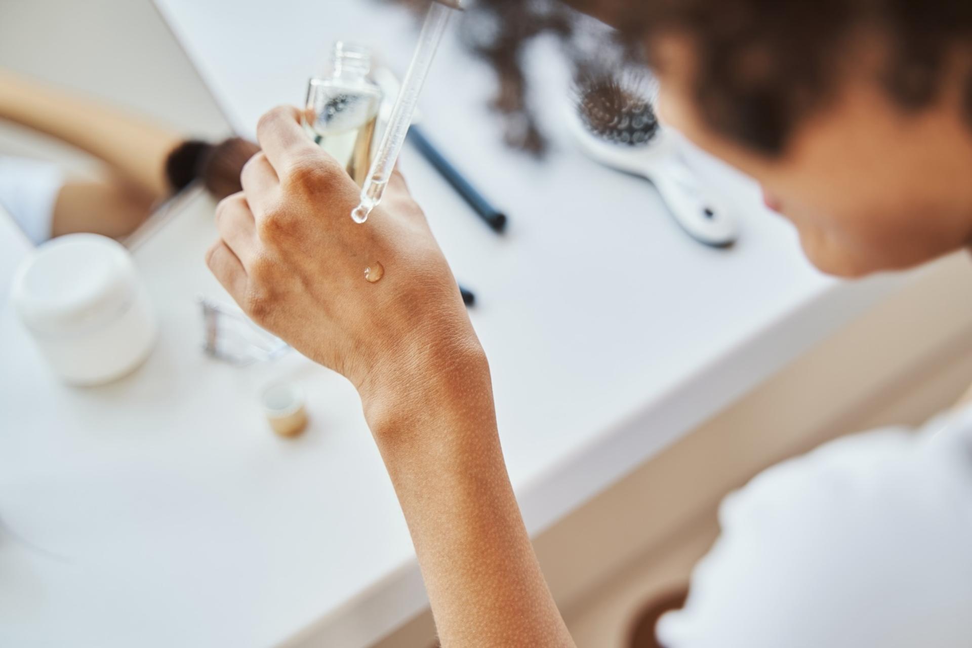 A woman applies hyaluronic acid to her hand with a dropper
