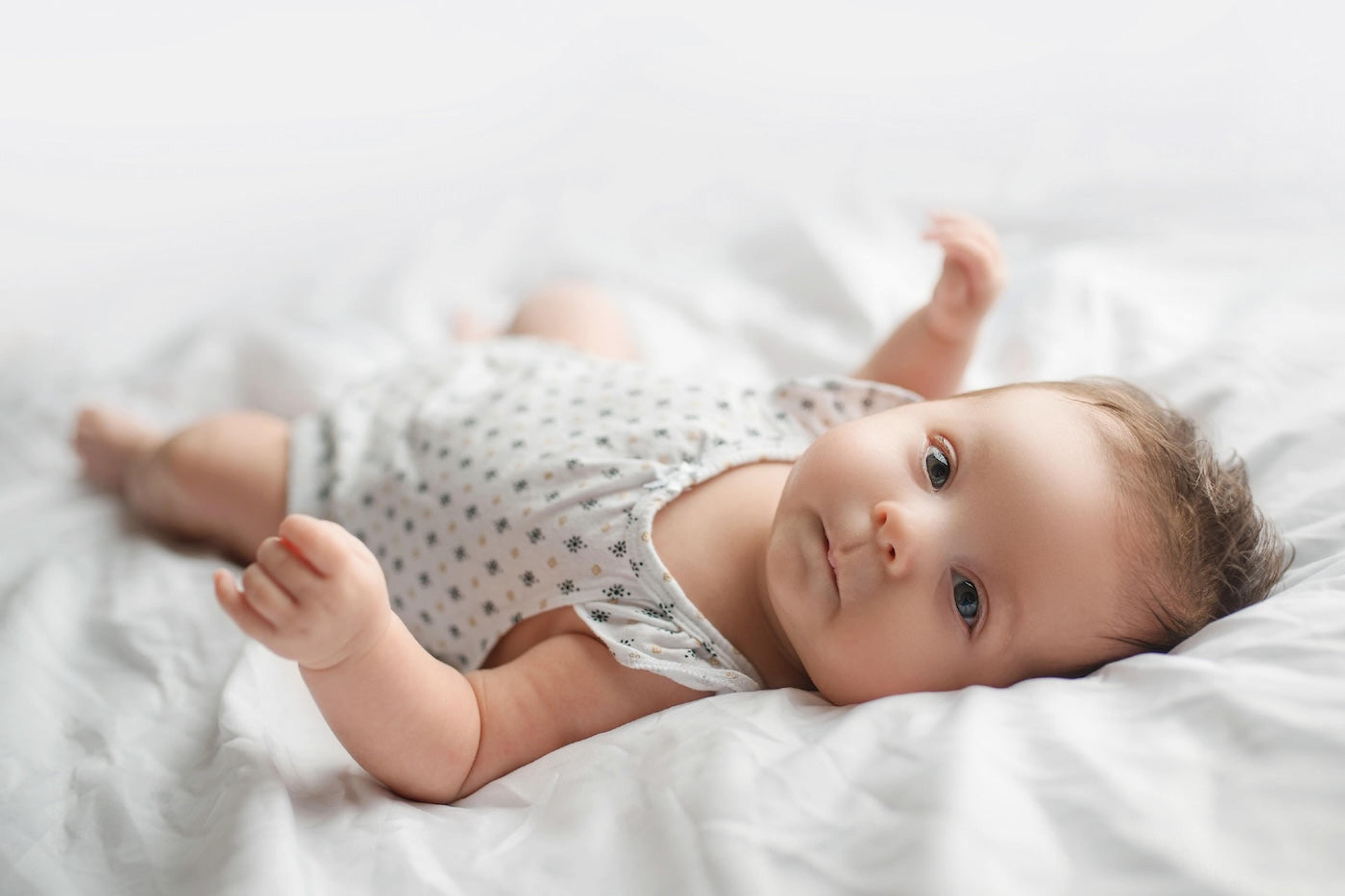 A 9-week-old baby lays on a bed