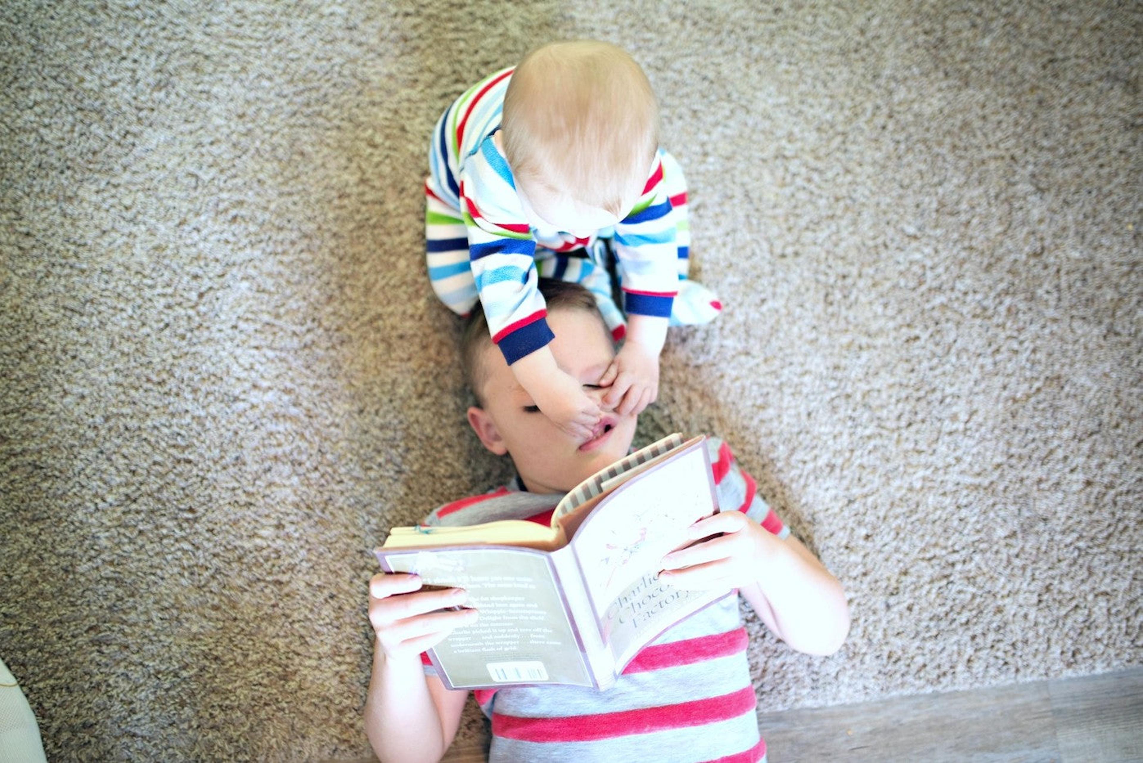 A baby pinches and pulls at his big brother's face