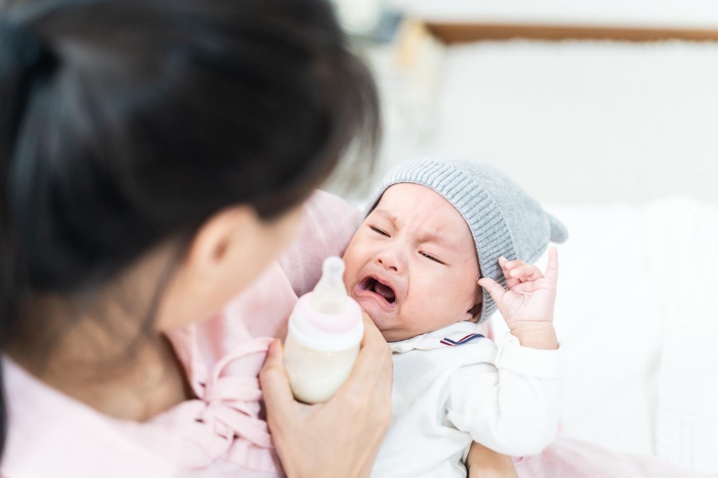 A mom tries to feed a crying baby a bottle