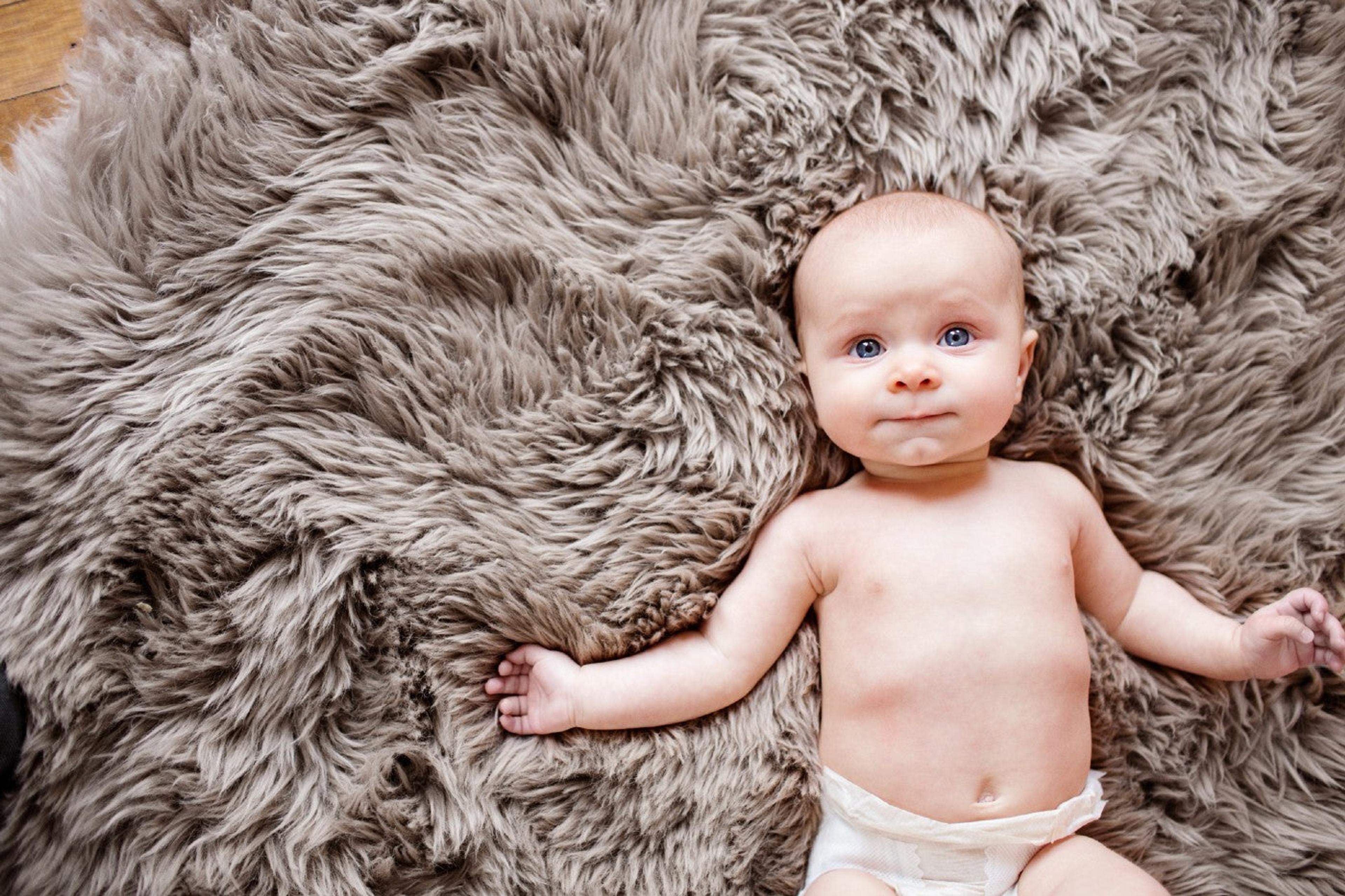 A baby lays on a soft gray nursery rug