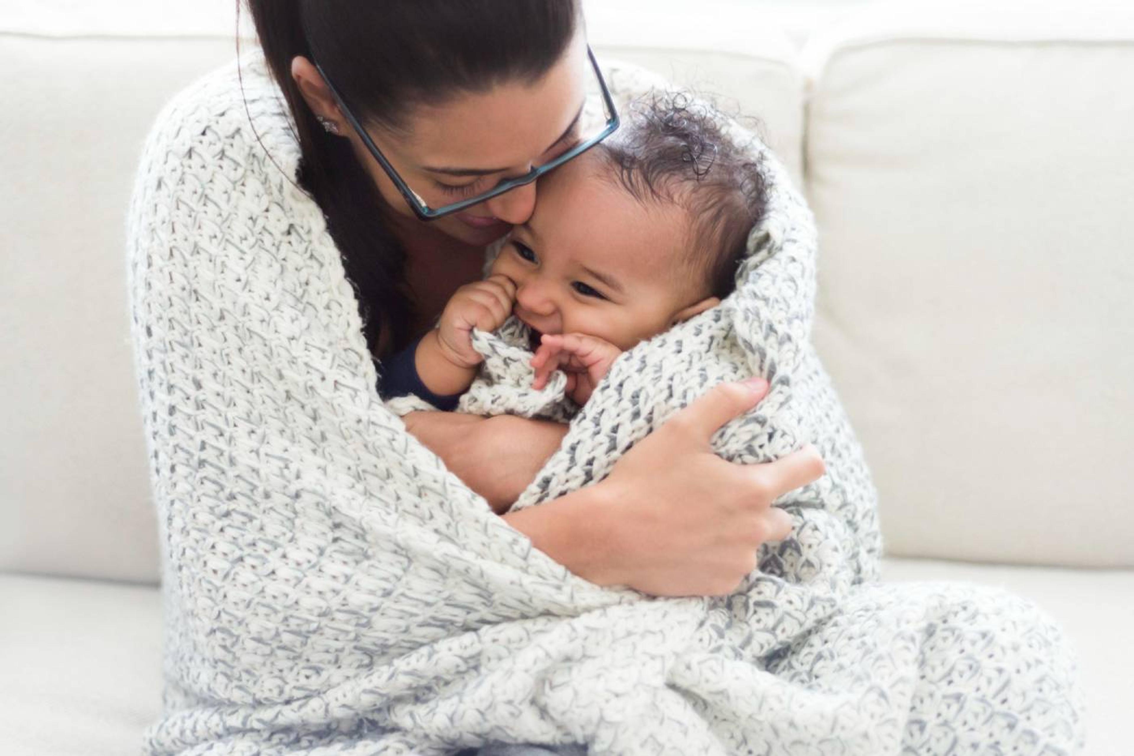 A mother snuggles her baby under a blanket
