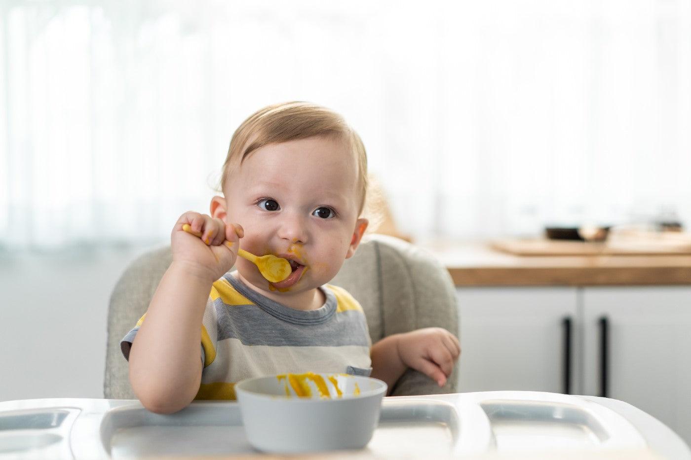 Baby boy eats sweet potato puree with a spoon